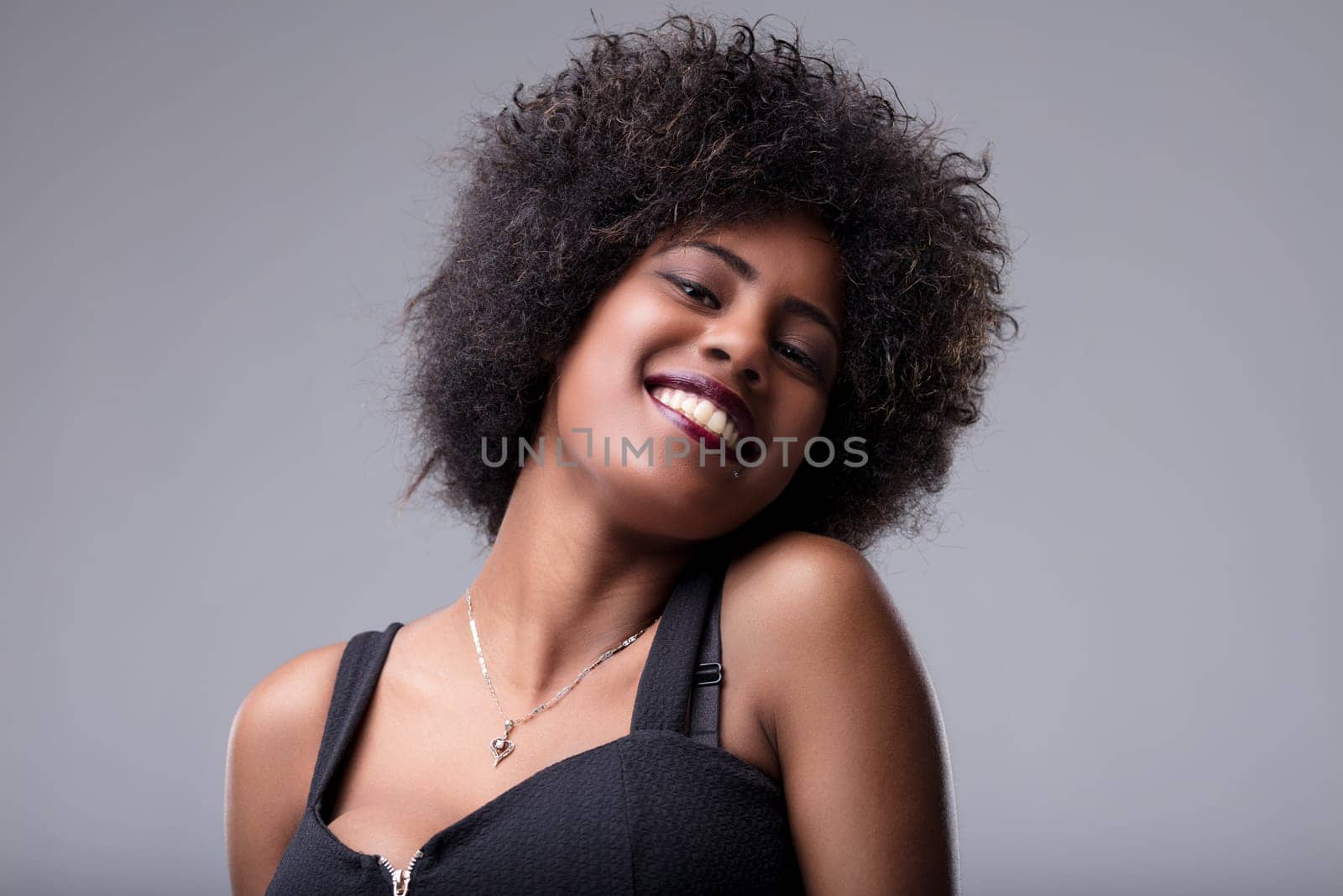 Young woman with curly afro hair and a radiant smile posing for a studio portrait, exuding happiness and confidence while looking directly at the camera