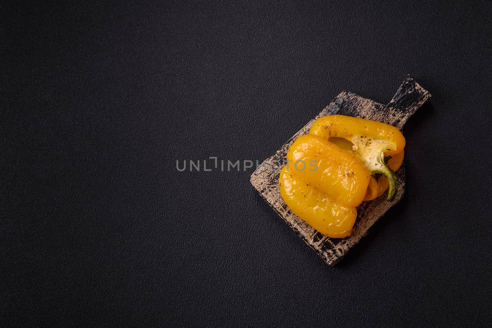 Yellow sweet pepper cut in half and grilled with salt, spices and herbs on a dark concrete background