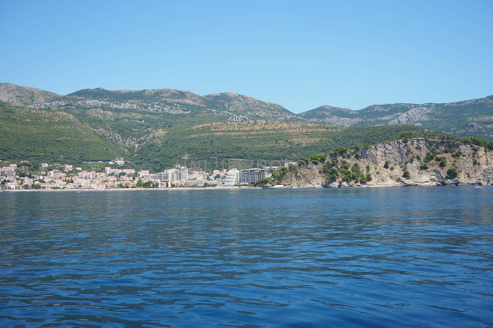 Petrovac, Montenegro 07.22.24 A boat ride past shore with vacationers, sunbathers and swimmers. Hotels, sun umbrellas, Adriatic waves, buoys. Beach tourism. Vacation travel. Summer day. Sandy pebble.