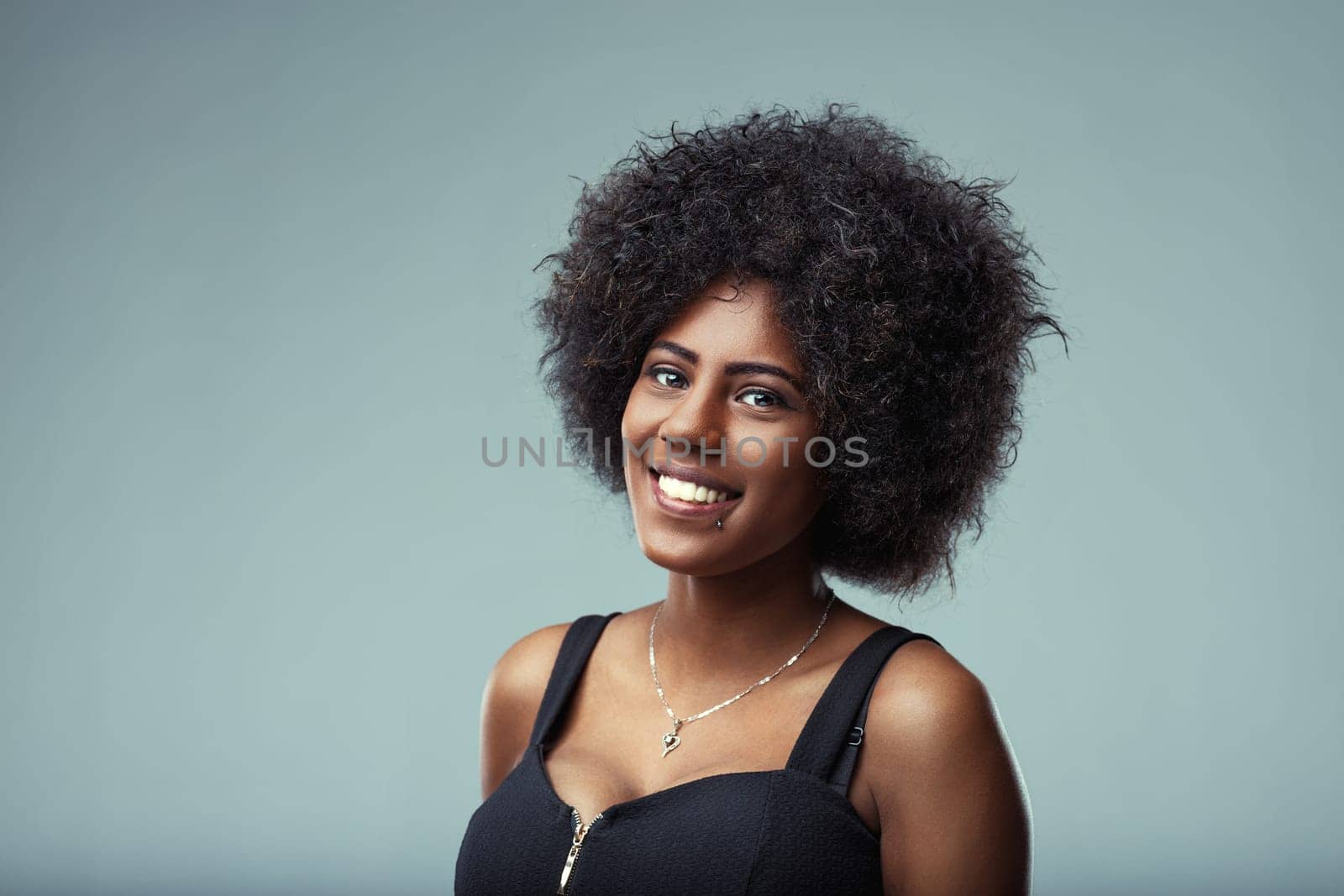 Studio portrait of a cheerful young latin american woman with curly hair, smiling confidently and expressing happiness against a light blue background