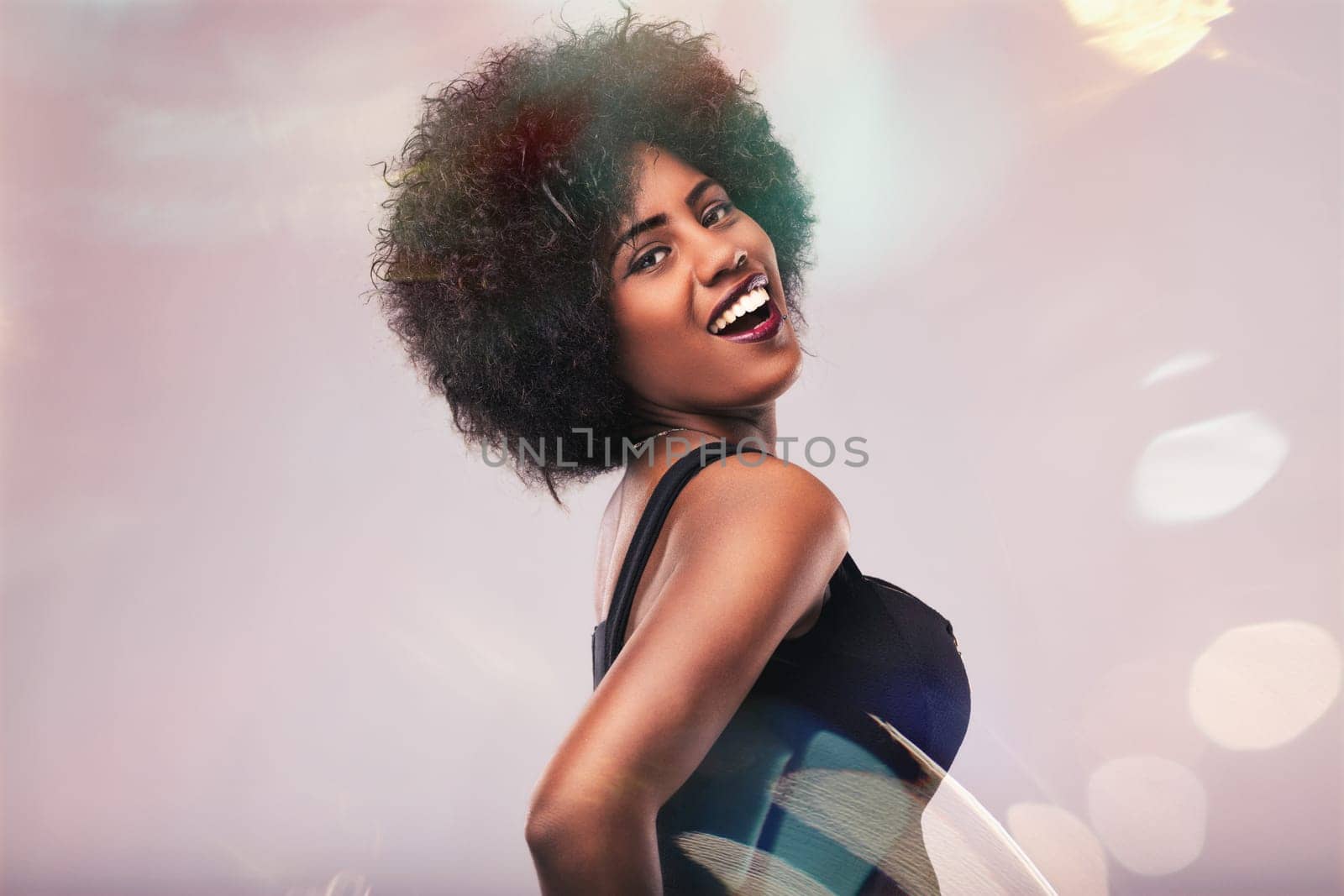 Young woman with beautiful afro hair smiling and dancing joyfully, surrounded by a vibrant bokeh effect in the background, capturing the essence of celebration and happiness