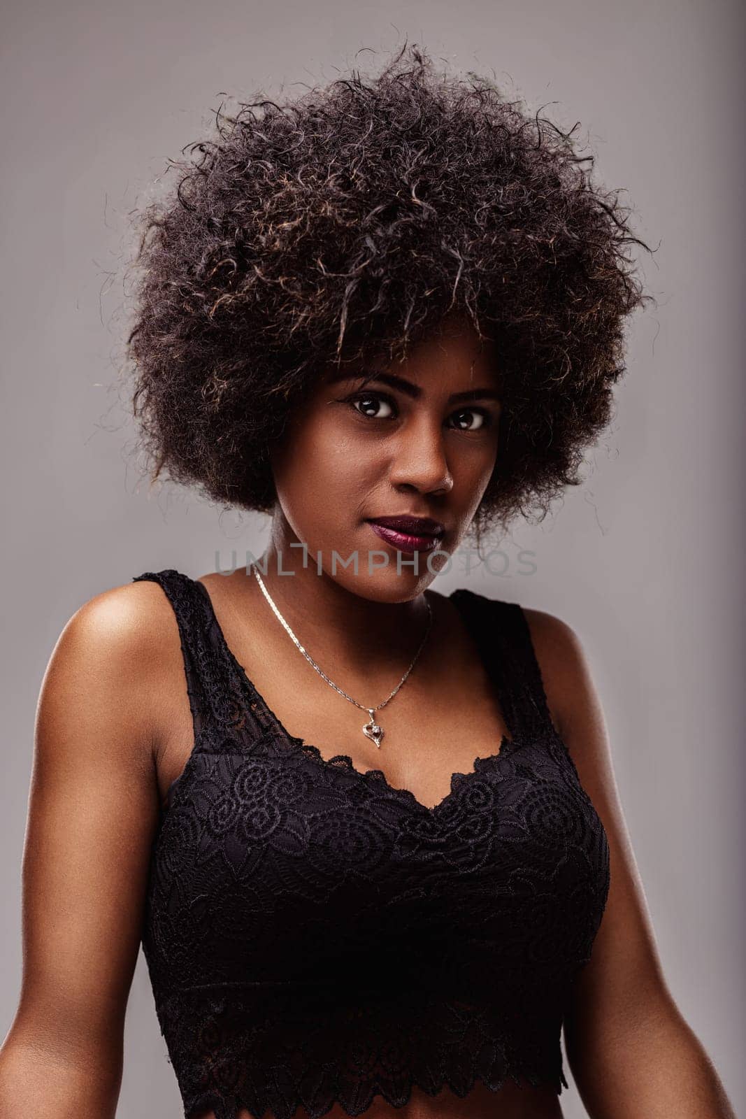 Portrait of a beautiful young african american woman with curly hair and dark skin wearing a black top and silver necklace, looking directly at the camera with a confident expression