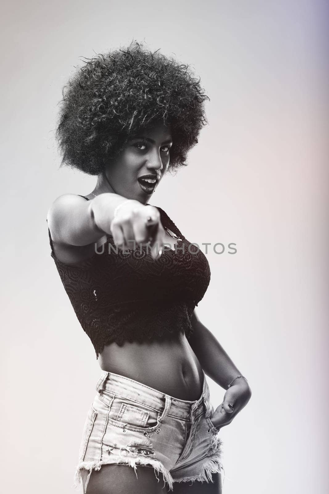 Black and white portrait featuring a young woman with striking afro hair, confidently pointing her finger while engaging directly with the camera, exuding self-assuredness and style