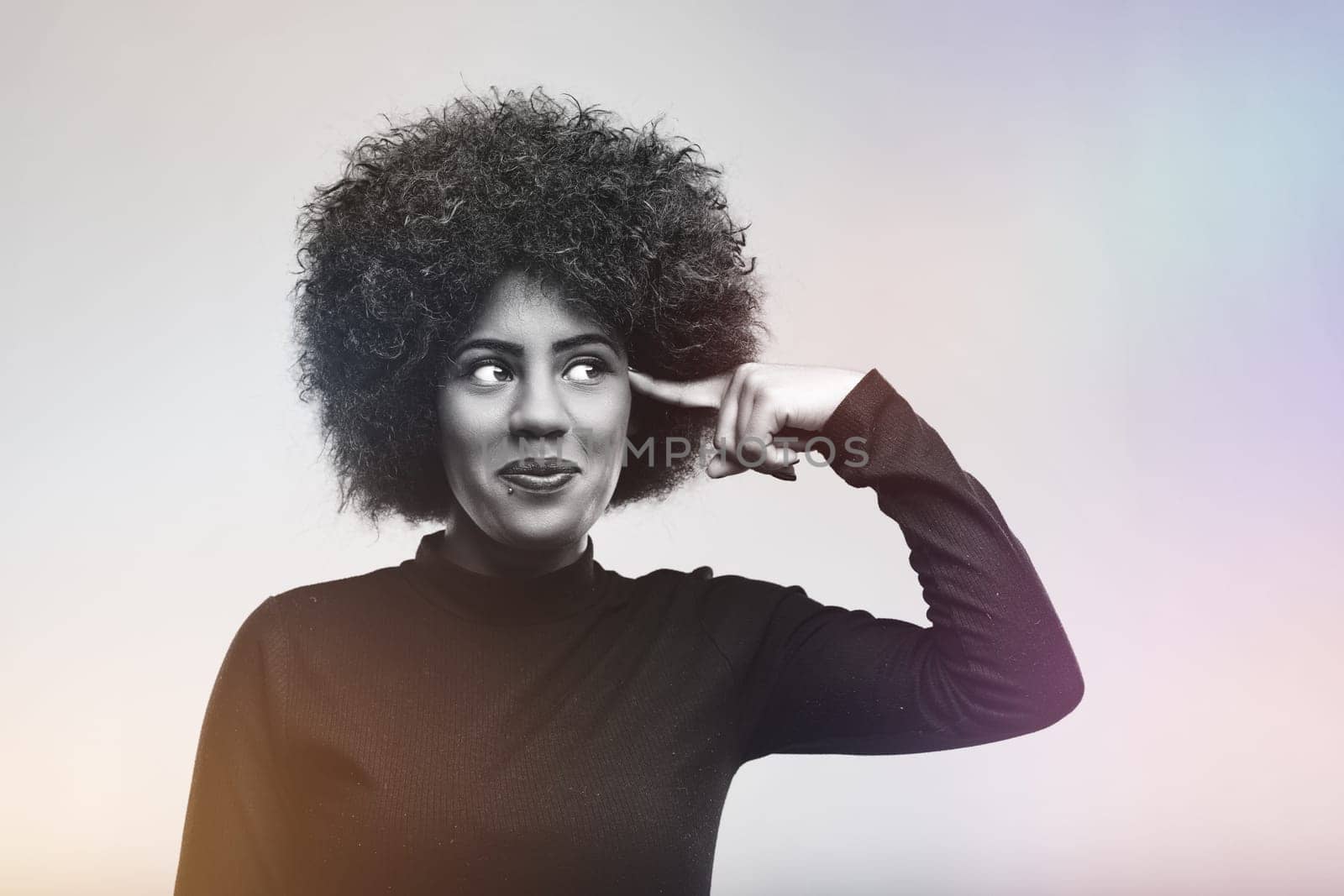 Studio portrait of a young woman pointing her finger to her temple suggesting she is crazy or has a brilliant idea, looking up with a funny expression