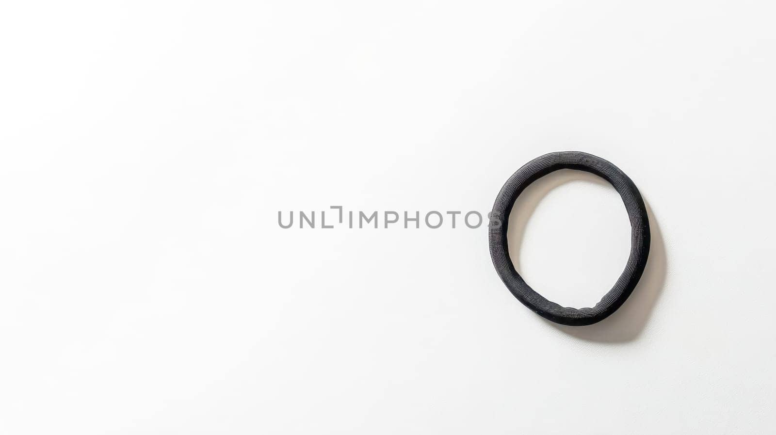 Plain black hair tie rests on a minimalist light background, creating a striking contrast and offering a clean, simple aesthetic perfect for beauty, fashion, or lifestyle projects