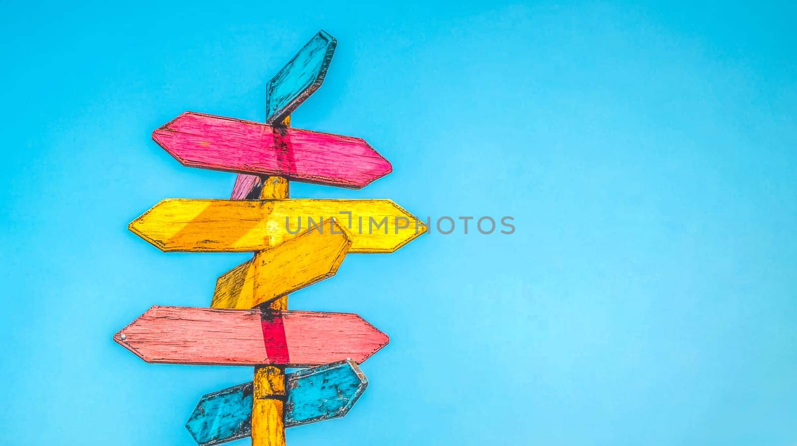 Wooden signpost with colorful arrows pointing in various directions against a vibrant blue sky, symbolizing choices, travel, and decision making
