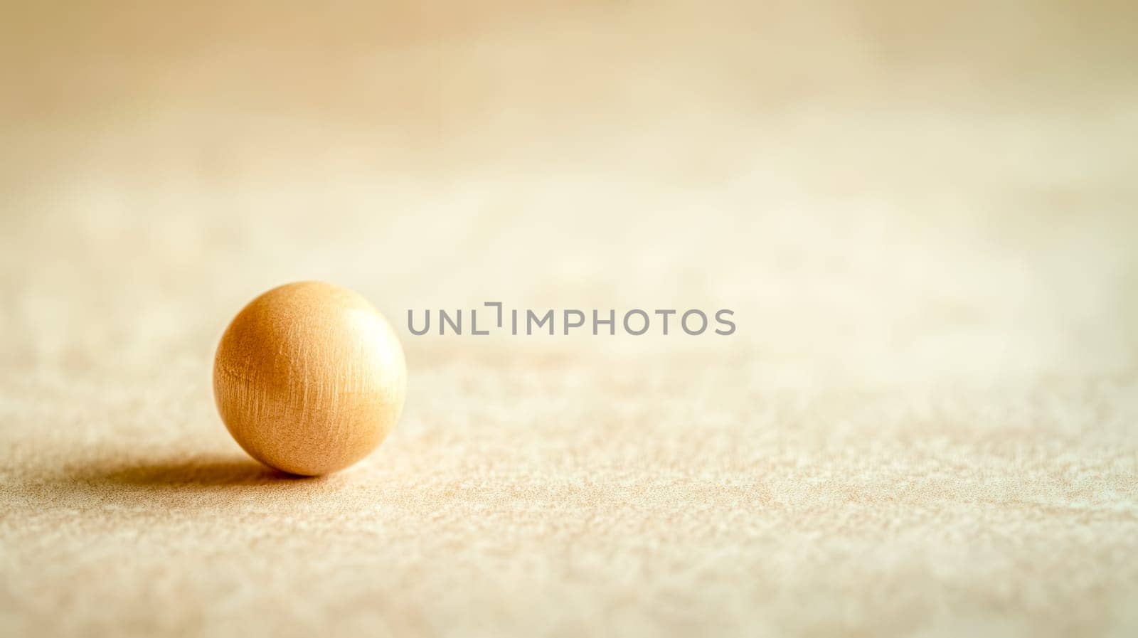 Small, smooth, light brown wooden bead resting on a light beige, textured background, creating a simple yet elegant composition with copy space