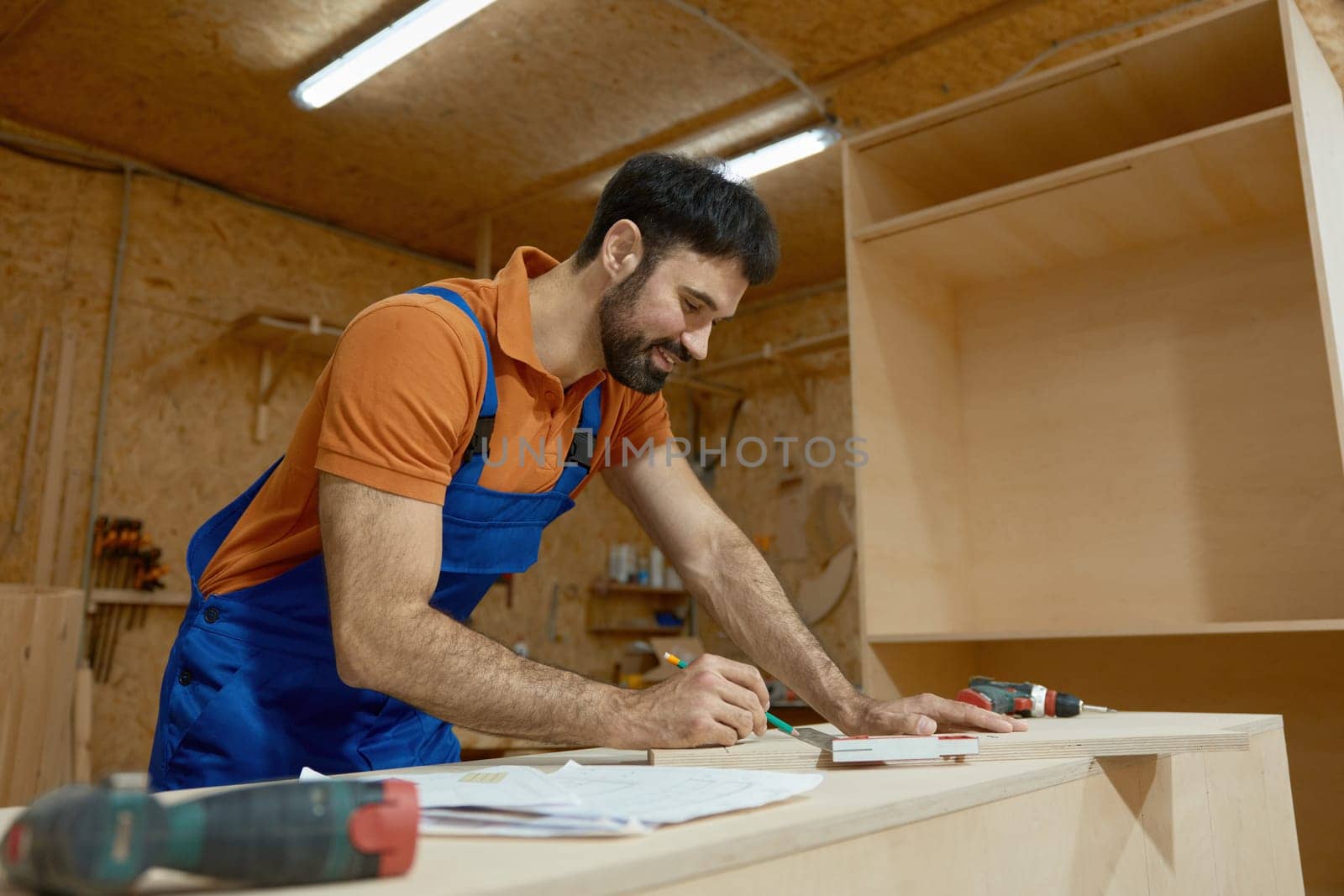 Carpenter doing wooden plank measuring with ruler during furniture construction process at workshop. Home renovation, remodeling project and woodworking concept