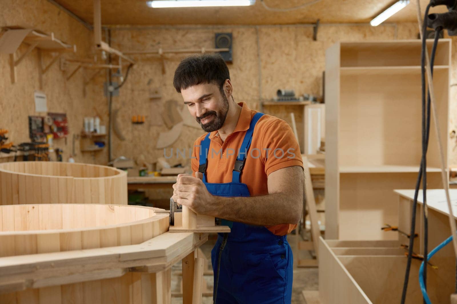Carpenter working on mini home wooden phytobarrel sauna at workshop. Artisan enjoying woodworking process creating compact steam room for customer