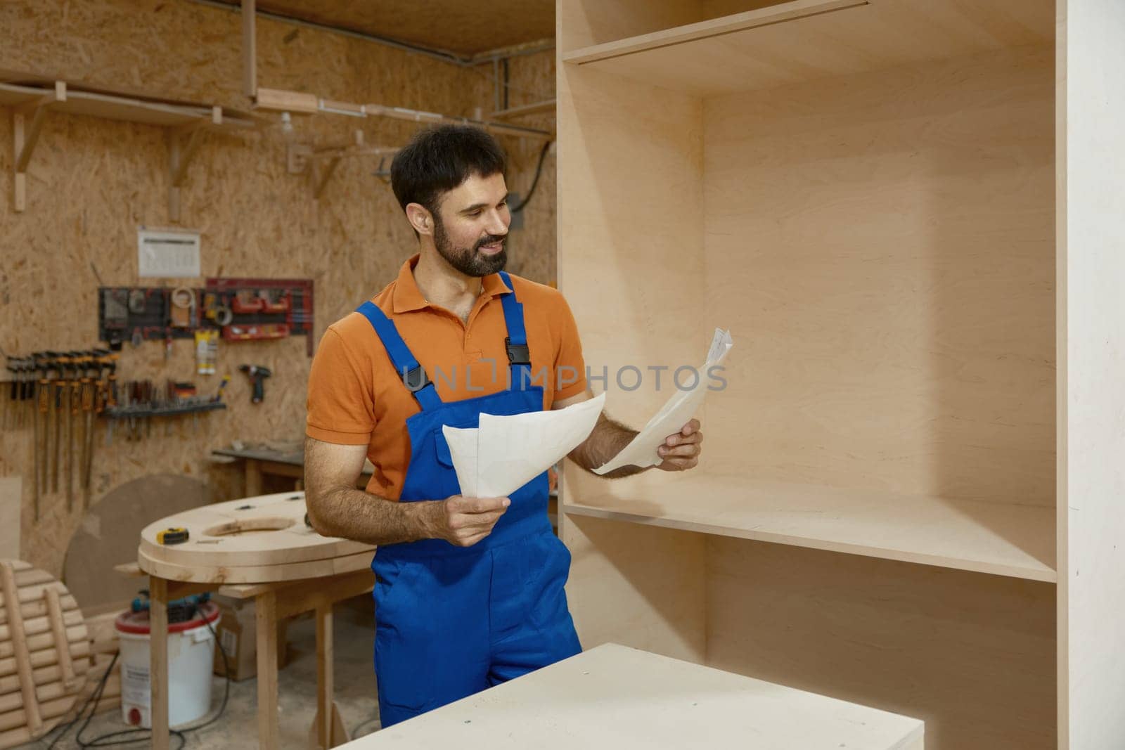 Carpenter looking at paper sheet with project blueprint reading assembly instructions standing over woodshop interior