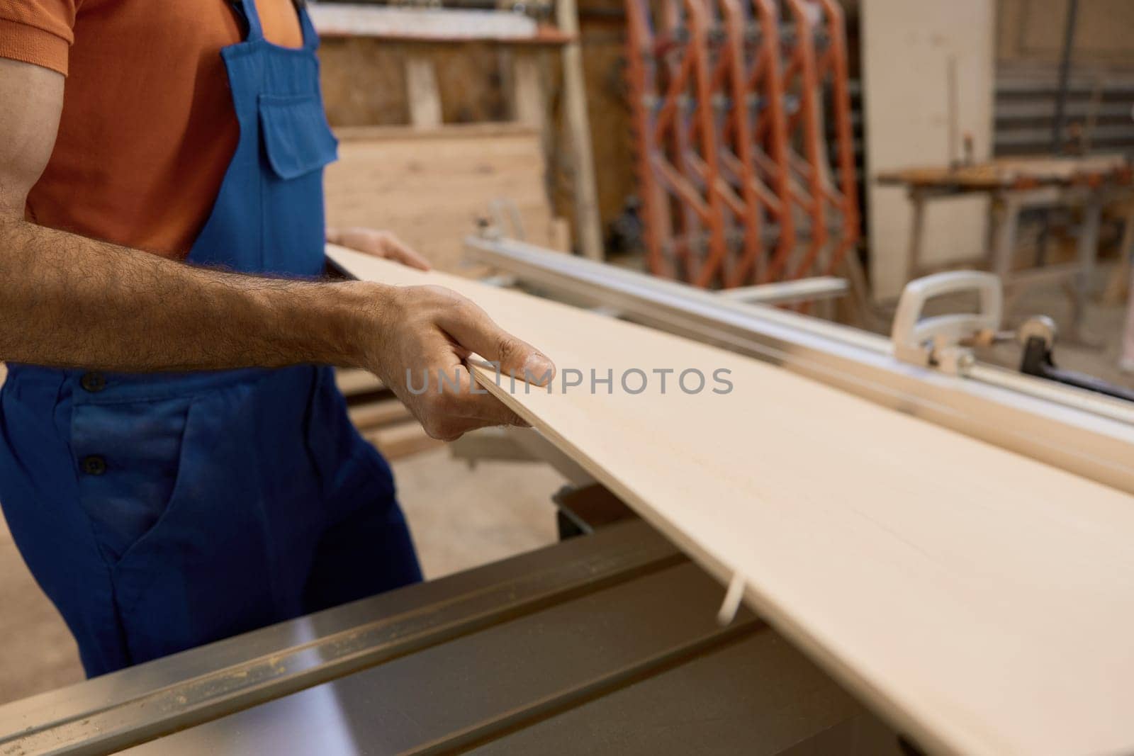Crop shot of craftsman in uniform and protective goggles cutting woods on pieces working at circular cutting table in furniture factory workshop