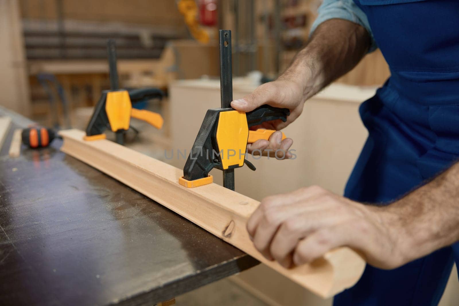 Carpenter fixing wooden plank on workbench with clamps carpentry tools while working at craft woodwork studio