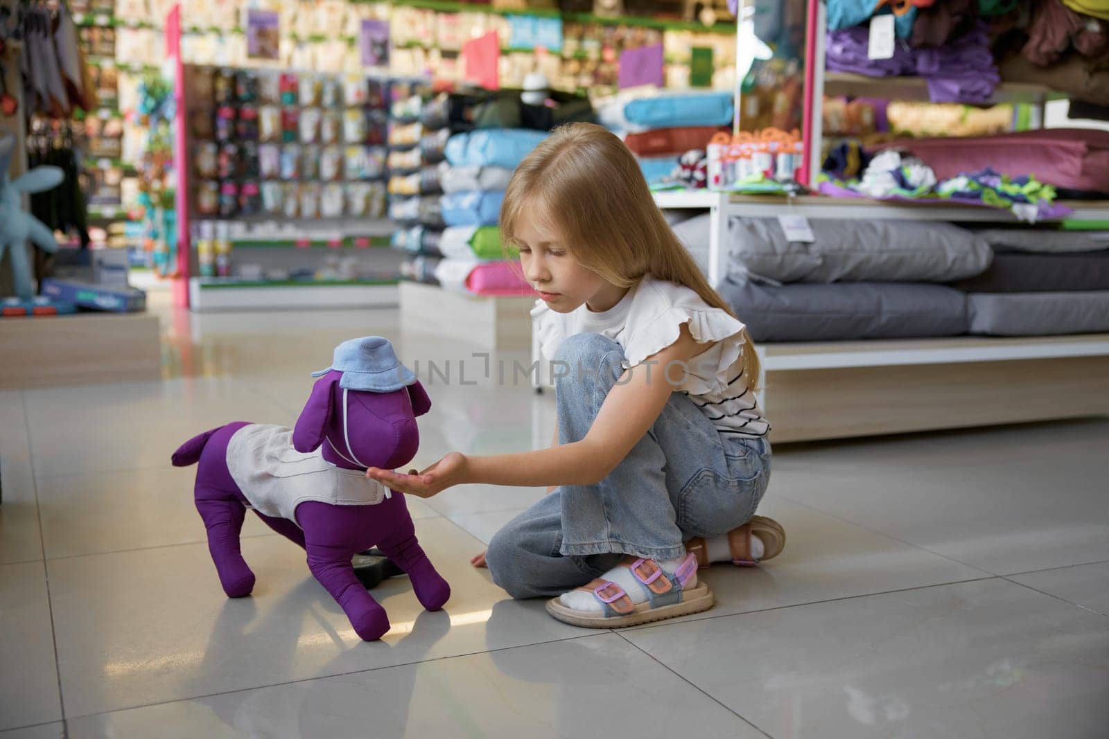 Little girl feeding toy dog sitting on floor of pet shop. Dreams of small female kid about domestic animal friend