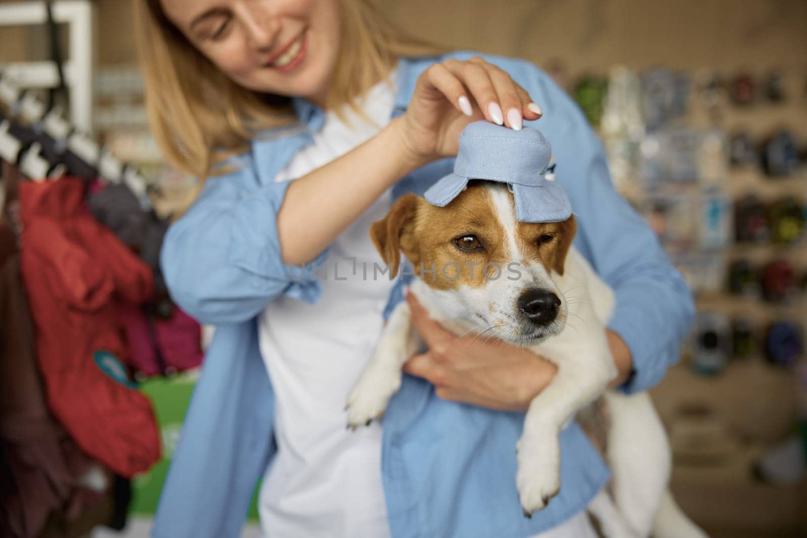 Young woman putting on cute costume hat on adorable dog head enjoying shopping at pet shop. Seasonal purchases for domestic animal