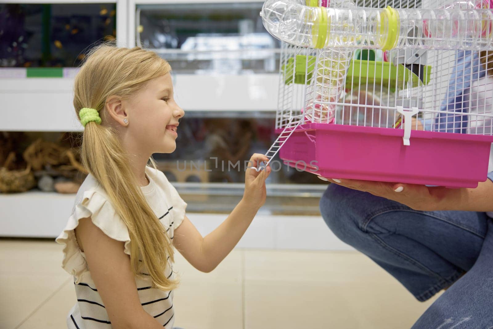 Cute daughter looking at new hamster cage in mother hands. Happy family shopping at pet store
