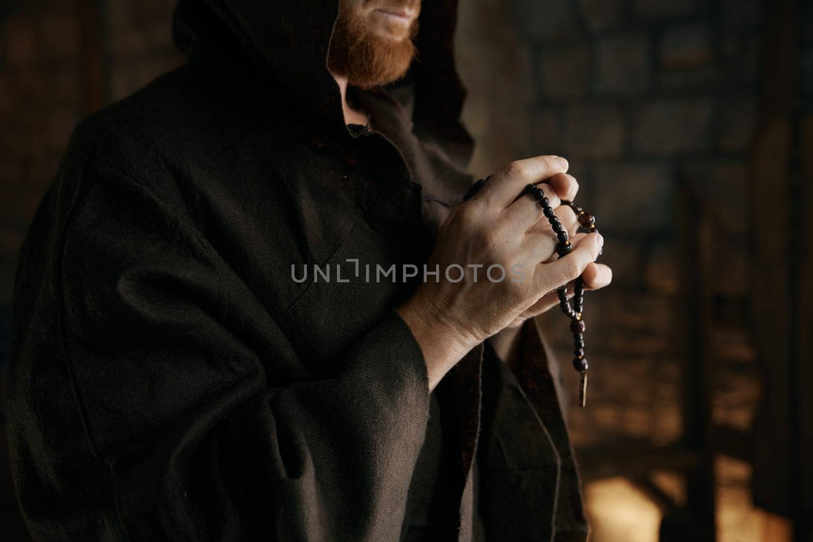 Cropped shot closeup of monk praying or blessing with rosary beads in hands standing over medieval monastery interior