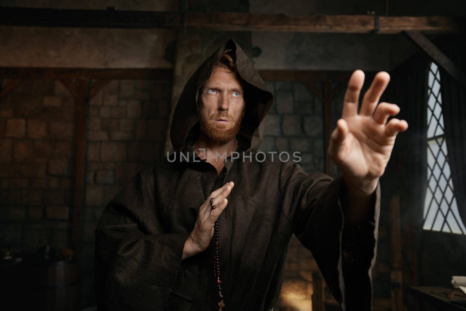 Portrait of friar wearing robe and golden cross reaching hand to camera. Monk demonstrating acceptance, forgiveness and attracting to faith