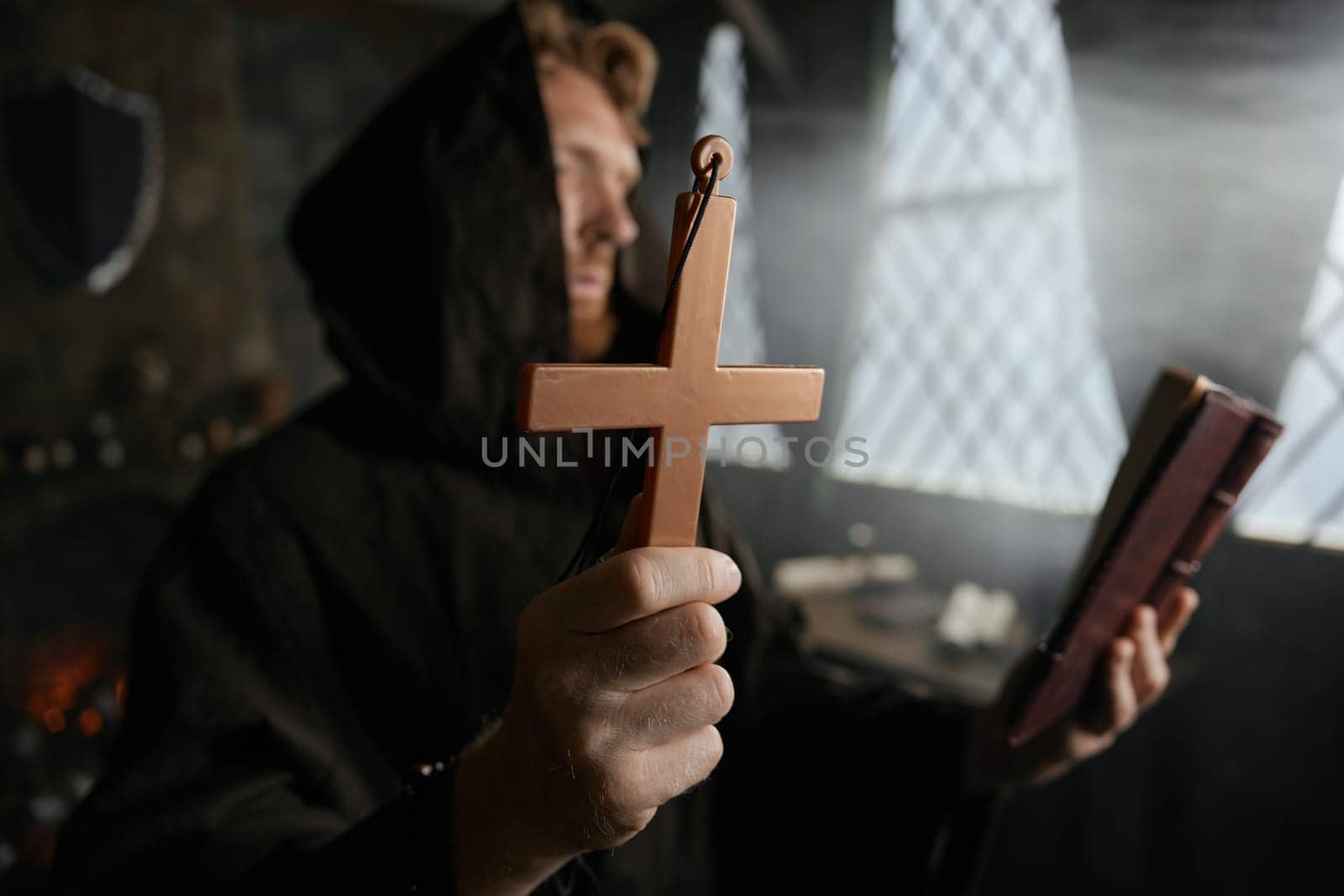Priest holding cross and holy bible reading prayer and performing exorcism rite selective focus