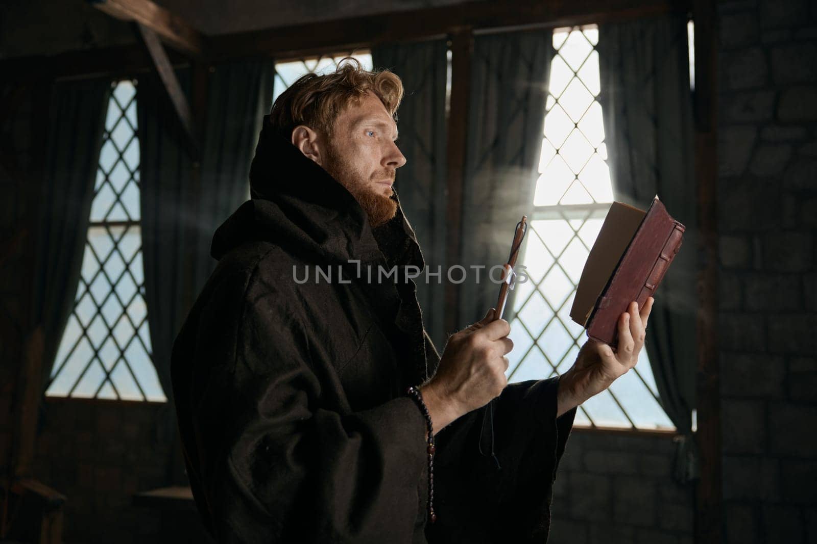 Medieval priest holding cross and holy bible reading prayer and performing exorcism rite selective focus