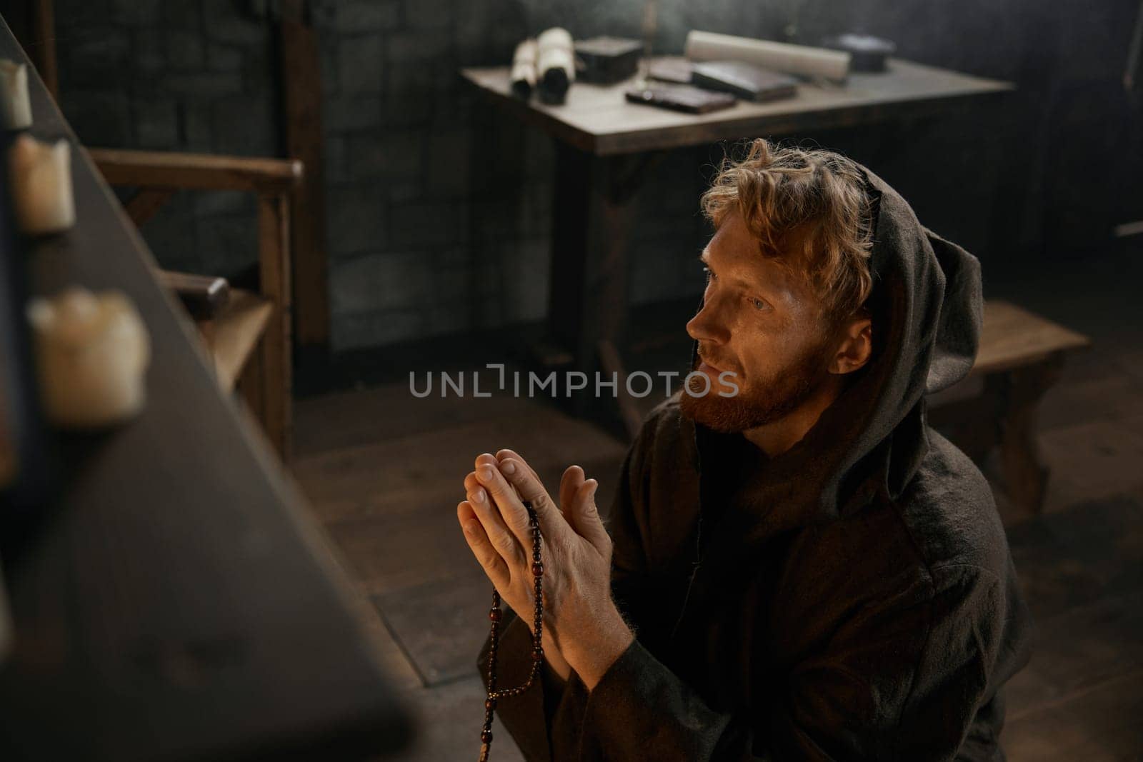 Desperate priest with folded praying hands kneeling before church altar in mystical smoke