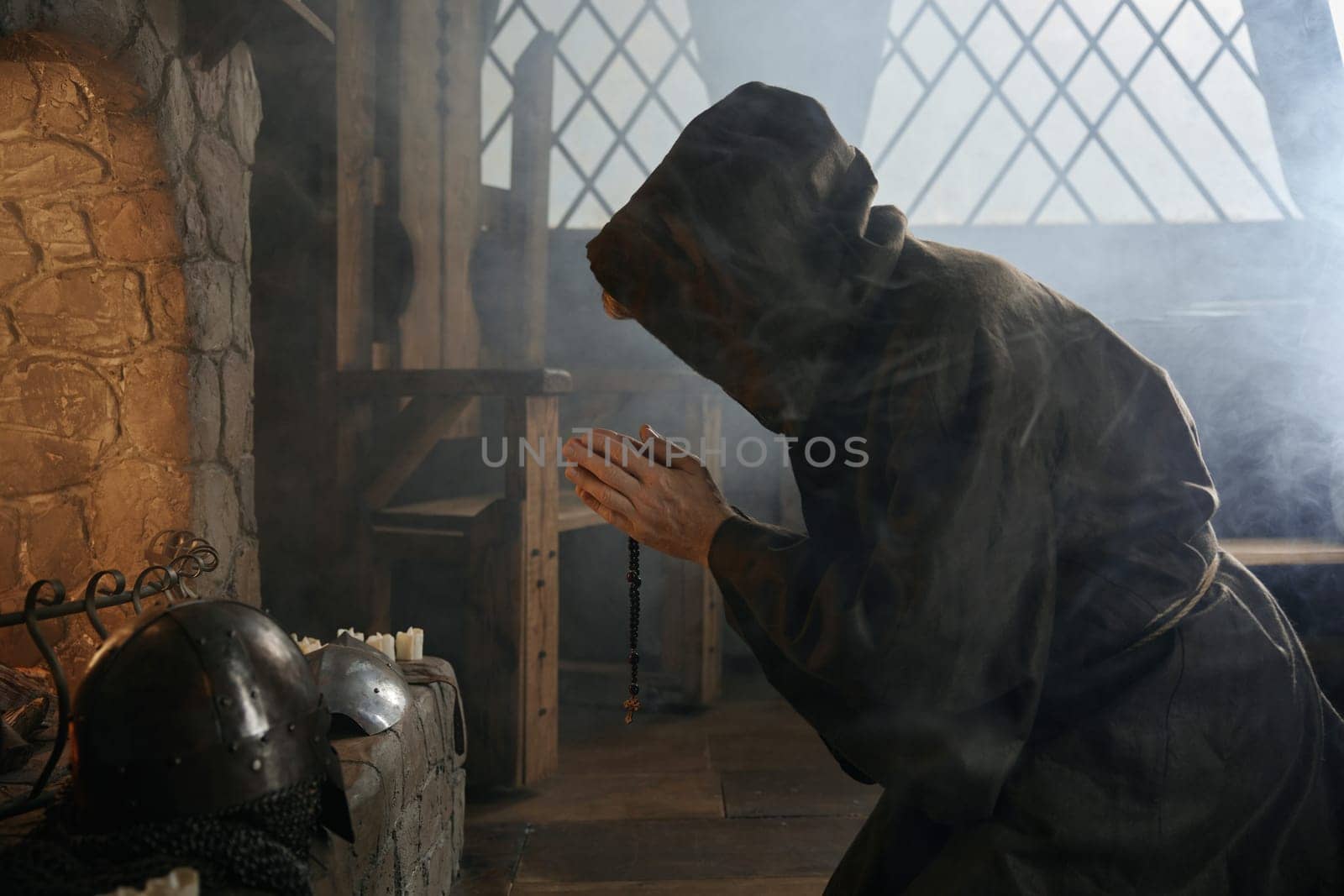 Desperate priest with folded praying hands kneeling before church altar in mystical smoke