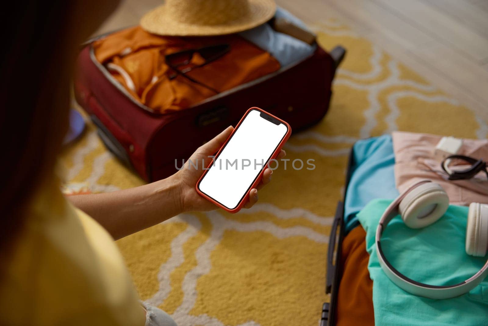 Empty blank screen on mobile phone in female traveler hand over opened luggage suitcase folded for vacation