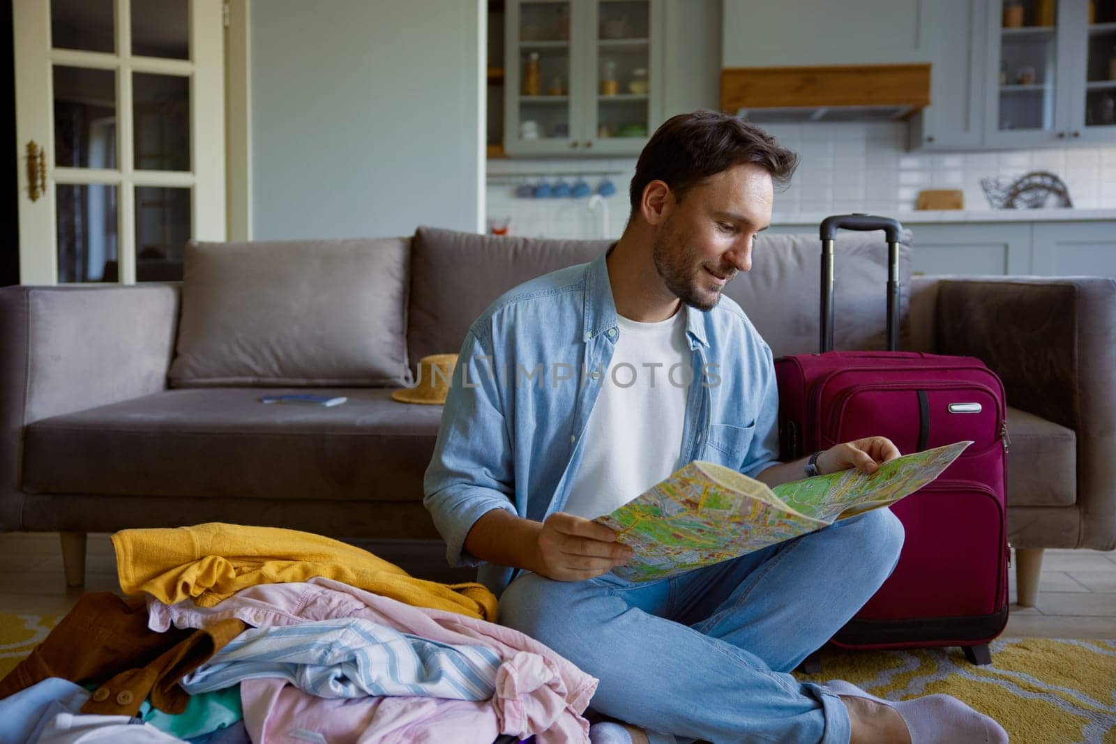 Young man tourist searching place of destination for travel reading paper map sitting on sofa in home living-room