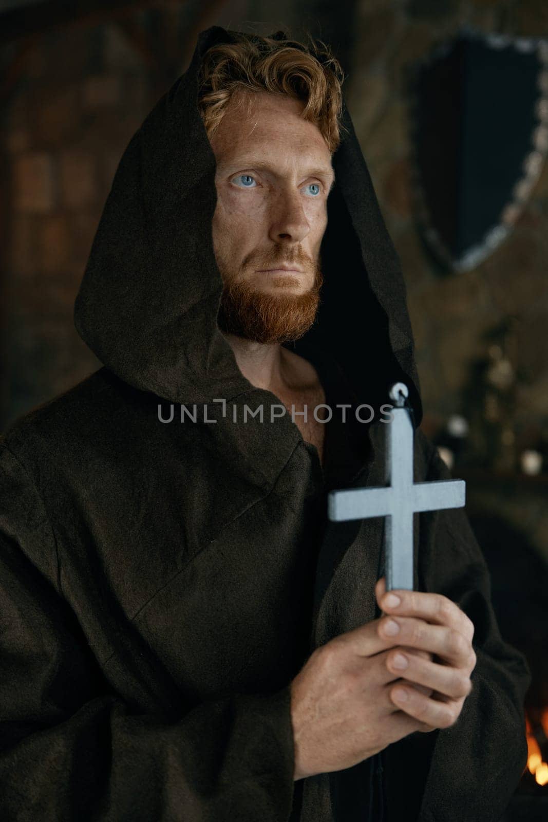 Medieval monk in robe praying holding silver cross in hand. Portrait of historic priest in monastery