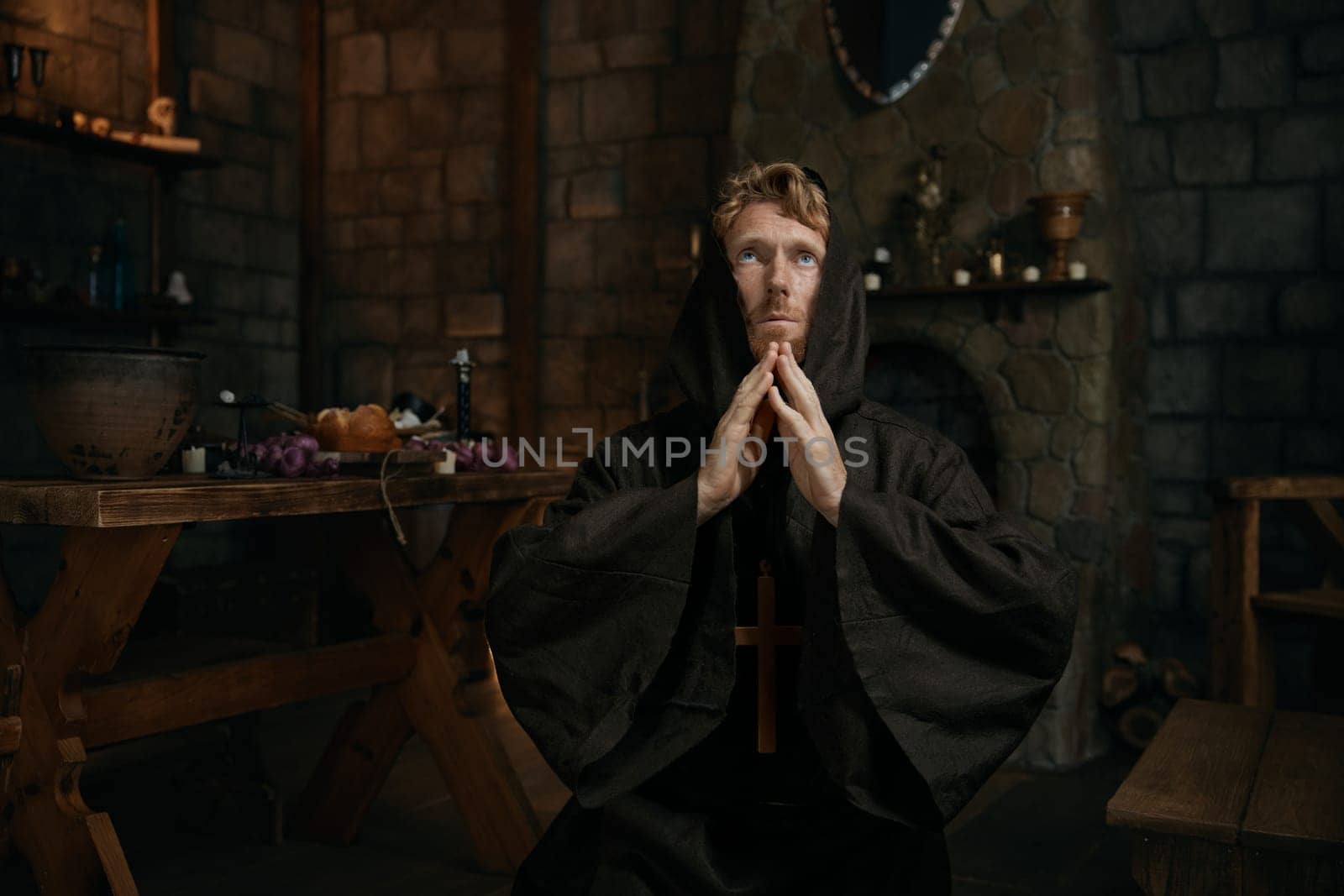 Desperate monk wearing robe wishing and praying to God looking upward in mediaeval monastery