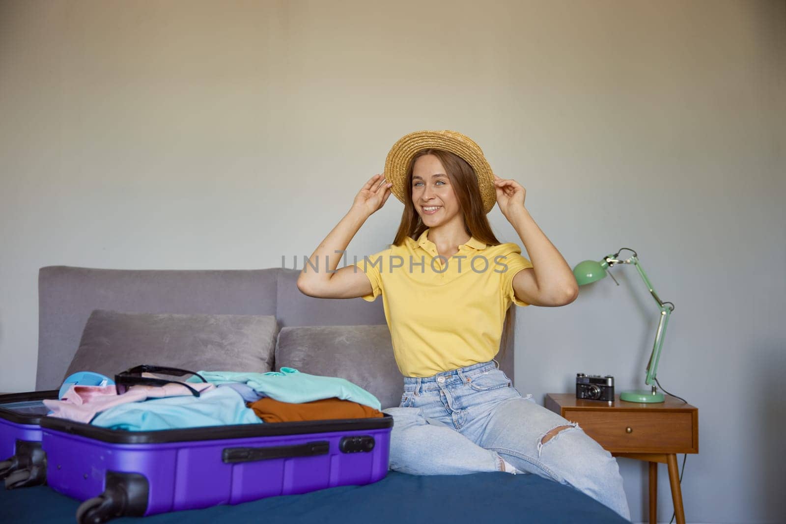 Joyful happy young woman rejoicing vacation time preparing suitcase luggage with clothes while sitting on bed at home