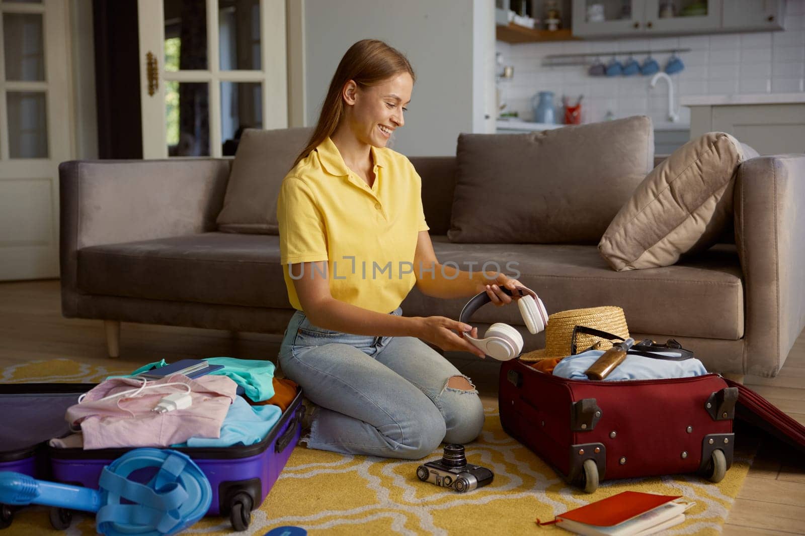 Young smiling woman tourist packing travel luggage putting headphones into bag with personal belongings