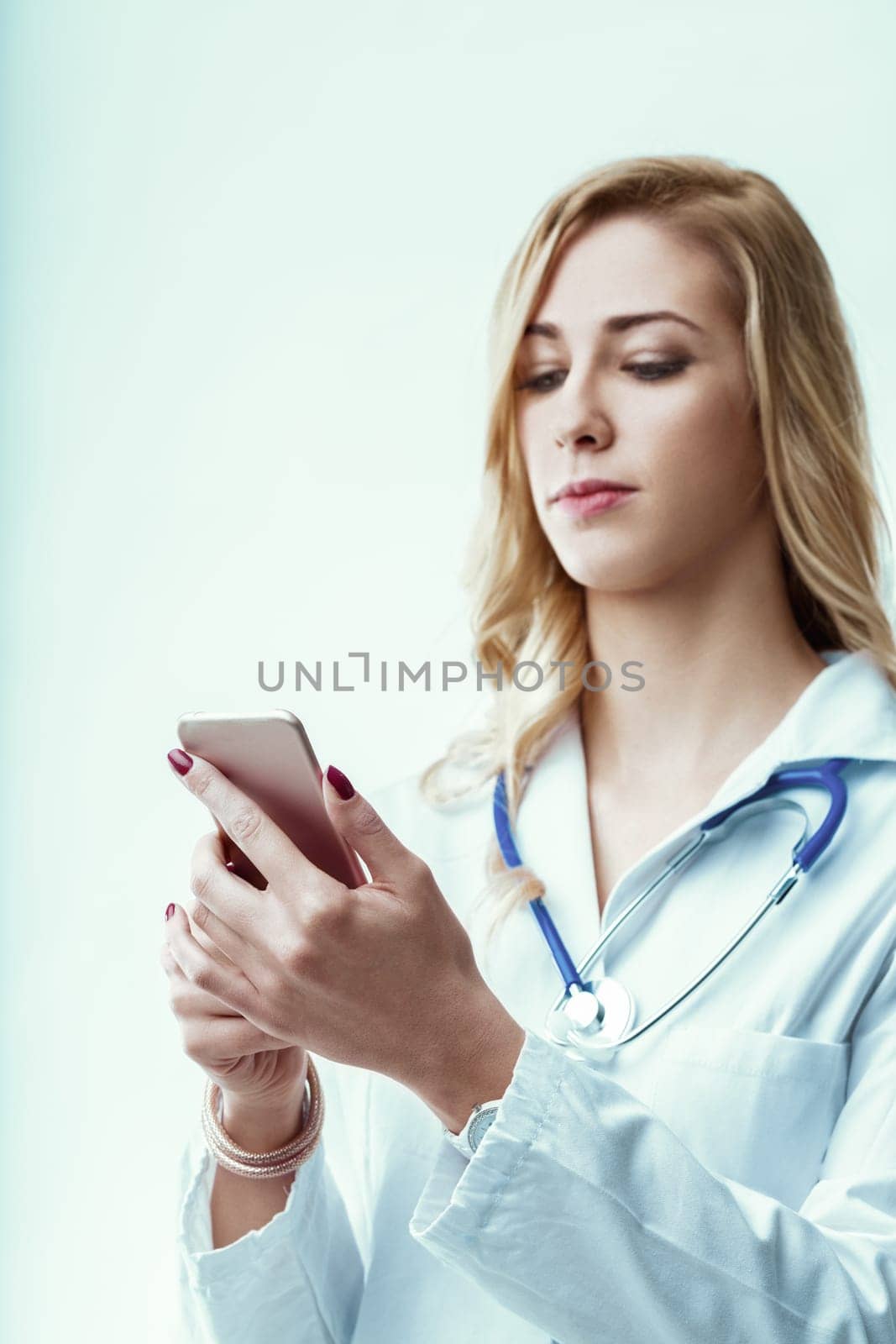 Young female doctor wearing a lab coat and stethoscope is engaged in reading medical news on her smartphone while navigating the fast-paced environment of the hospital