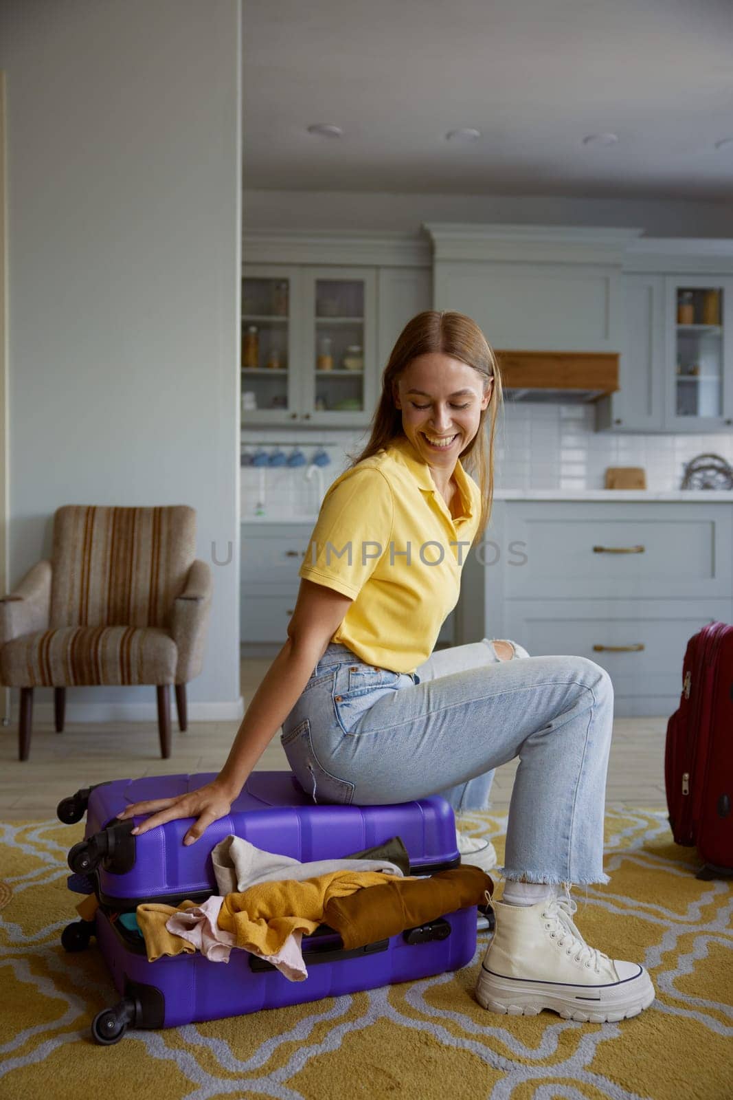 Happy overjoyed woman tourist sitting on overloaded travel suitcase with clothes excess. Summer vacation holiday preparation
