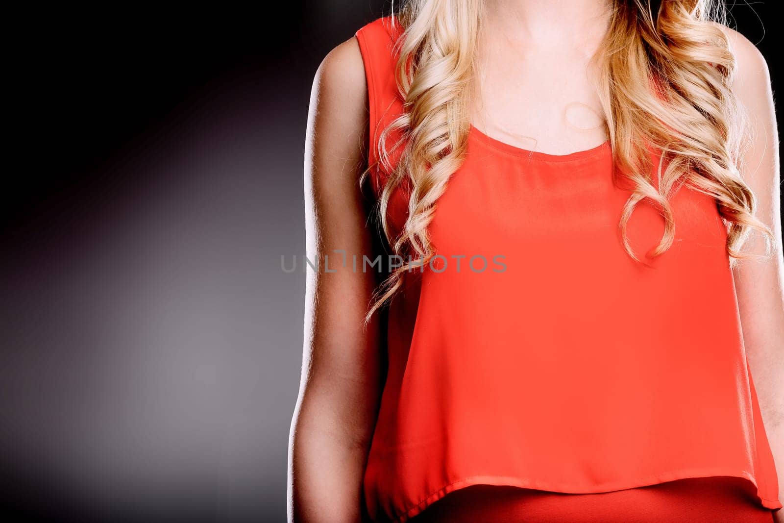 Close-up of a blond woman with curly hair, wearing a stylish red top, exuding confidence and elegance against a dark background, creating a visually striking image