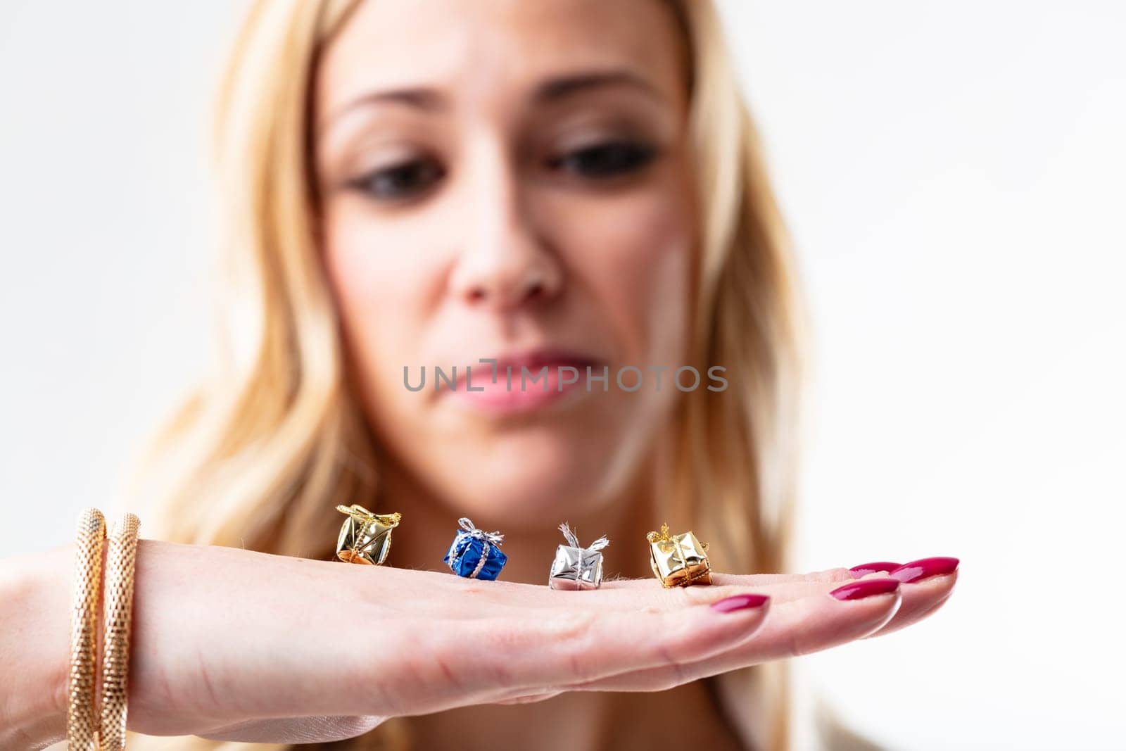 Four mini gifts rest on the hand of a young woman. Behind, blurred, her dissatisfied face. Maybe it's the thought that counts, but what's seen is the real gift, not the thought