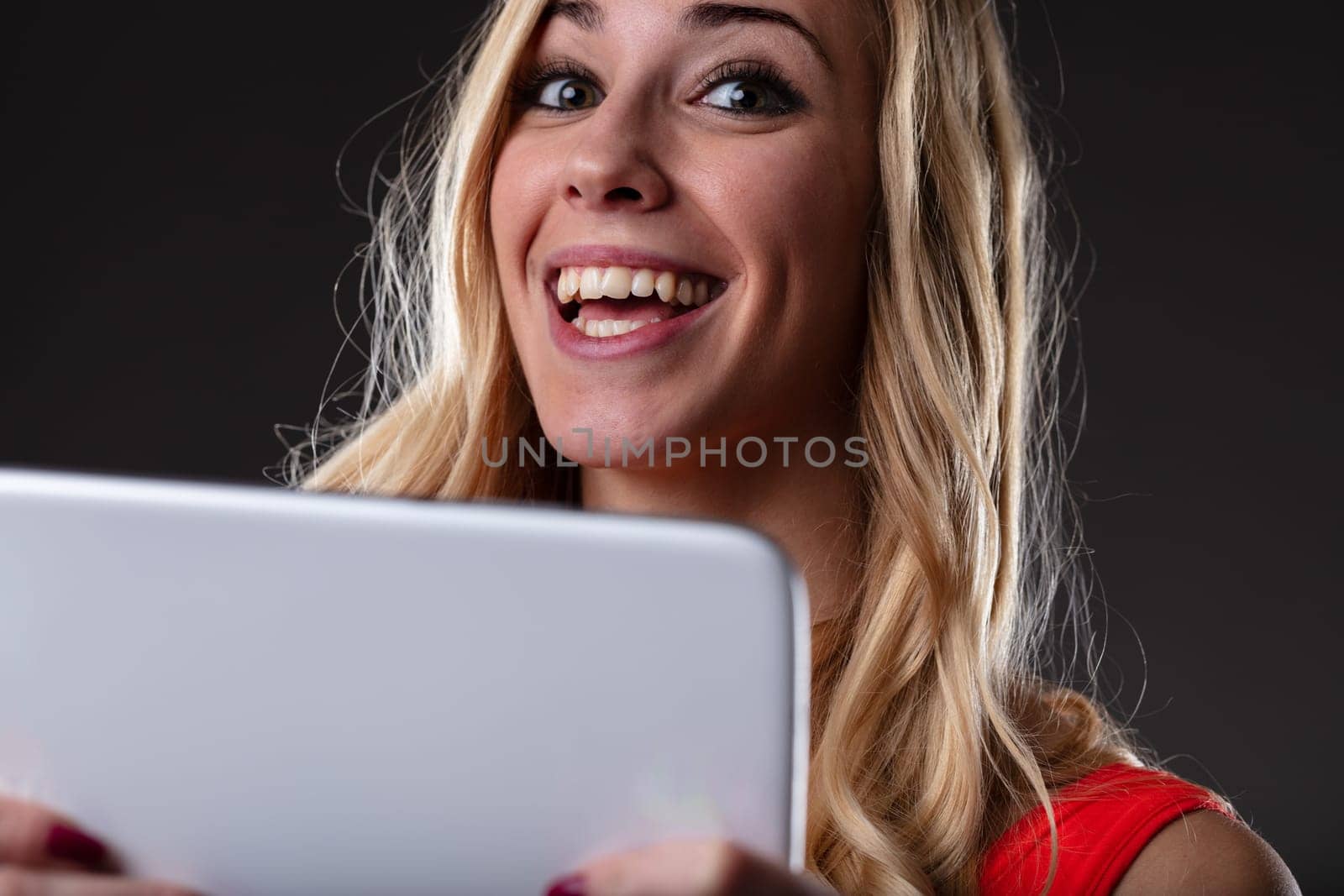 Happy young woman with a tablet excited about something online, be it a new series, shopping or great news. Dark contrasting background