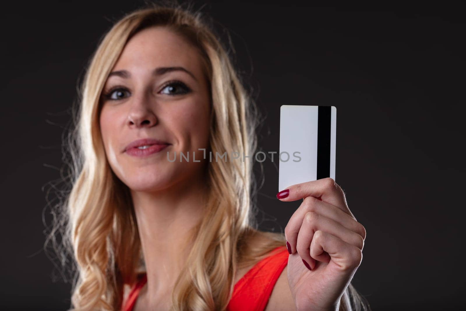 Excited woman with credit card ready for online shopping. Digital payments for convenience and speed. Blonde in orange, black backdrop, white card