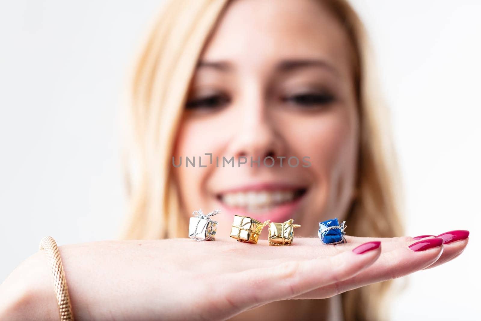 Four tiny gift boxes on a young woman's hand, in focus, with a blurred satisfied and smiling face in the background. Giving is as joyful as receiving
