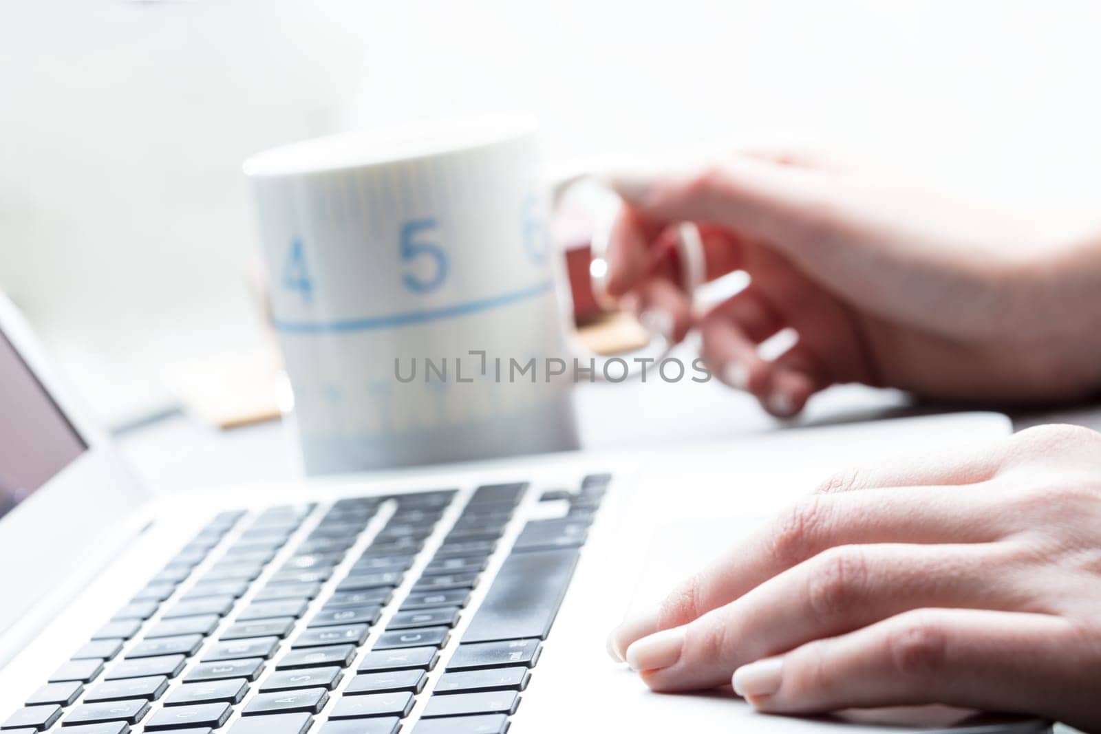 Businesswoman taking a coffee break at work as she sits at her laptop computer with shallow dof focus of her hands