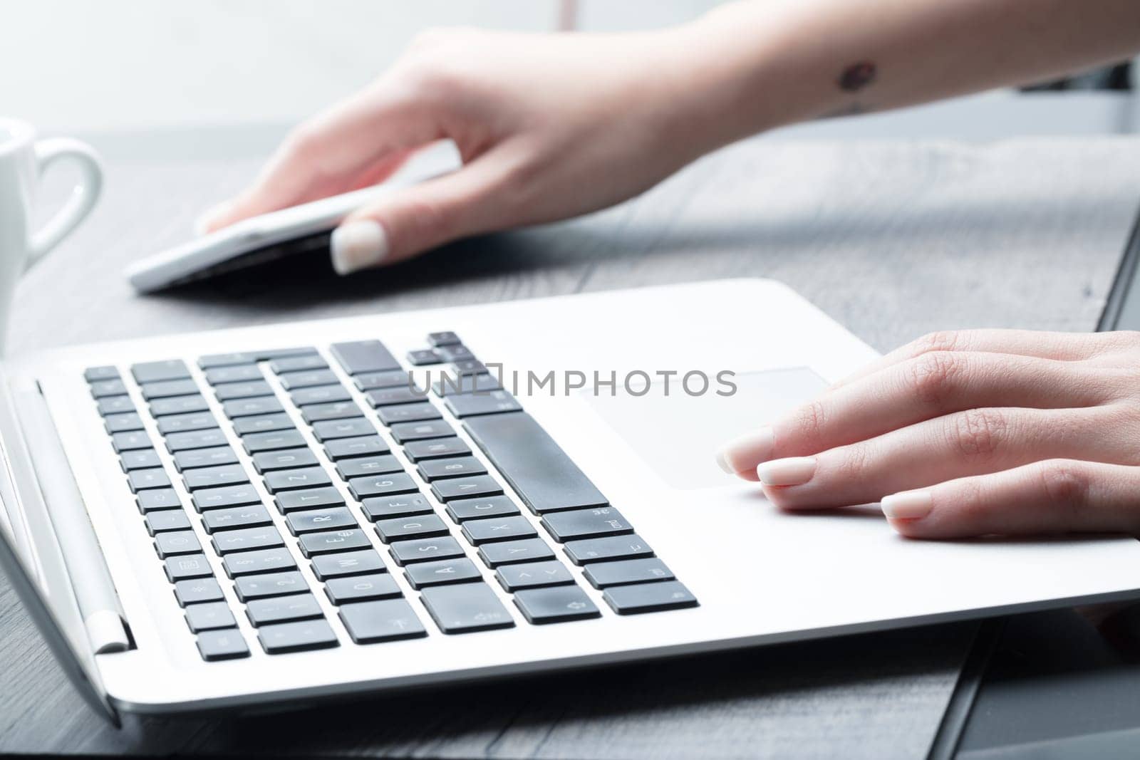 Businesswoman reaching for her mobile phone as she works on a laptop computer, low angle view of her hands