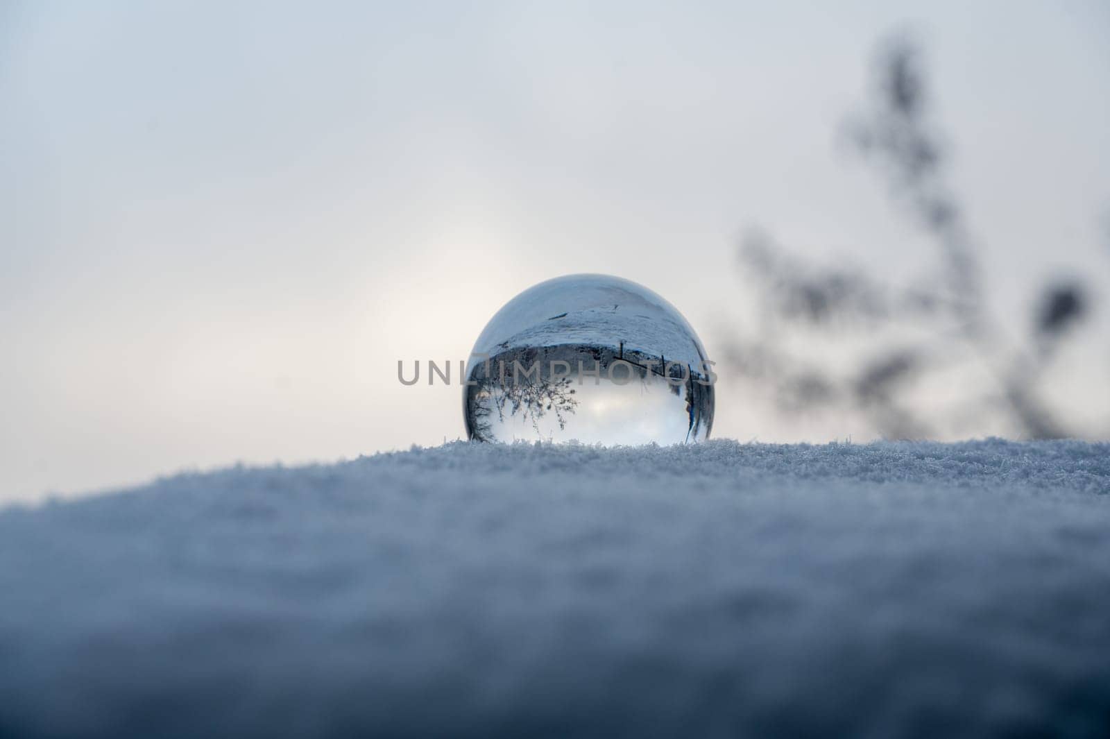Glass ball lying in the snow on a cold winter day, with reflections of snow-covered landscape in the glass