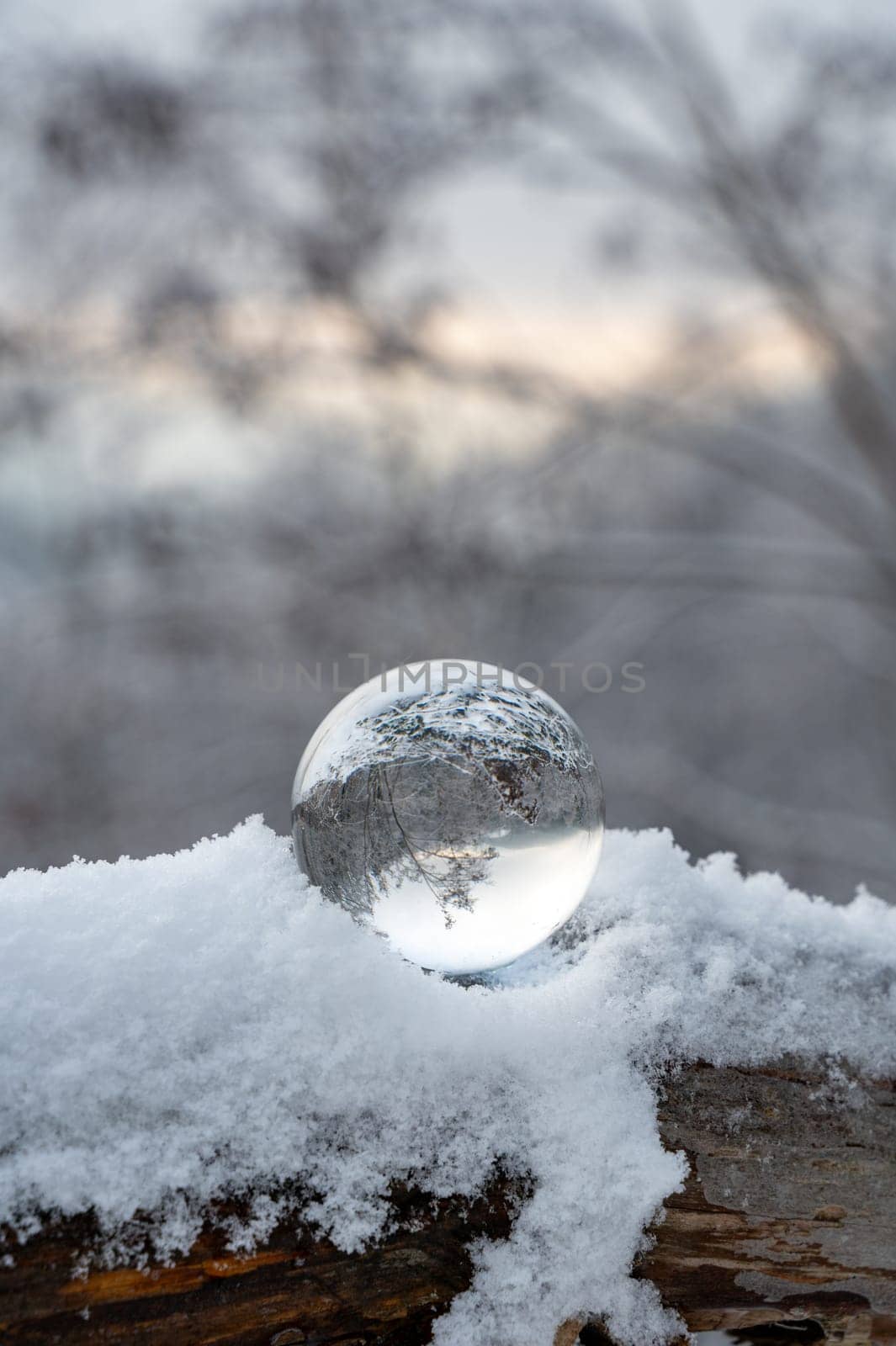 Glass ball lying in the snow on a cold winter day, with reflections of snow-covered landscape in the glass