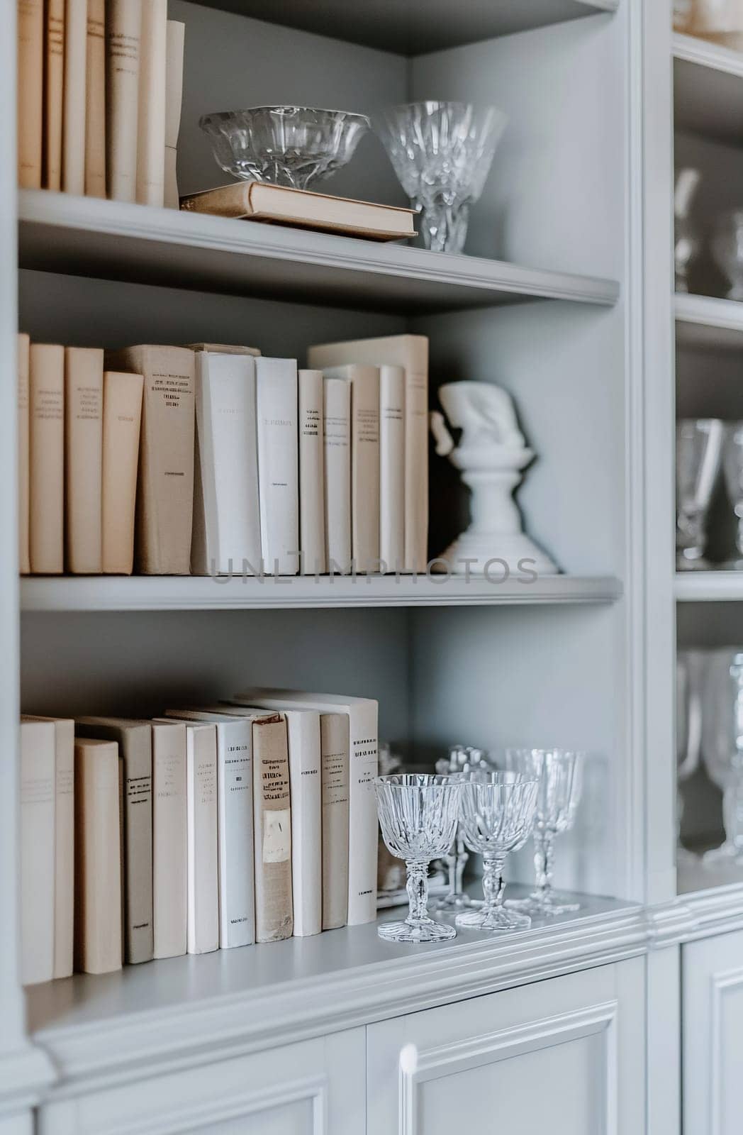 A well-organized bookshelf features neatly arranged books alongside elegant glassware, showcasing a blend of literature and decor.