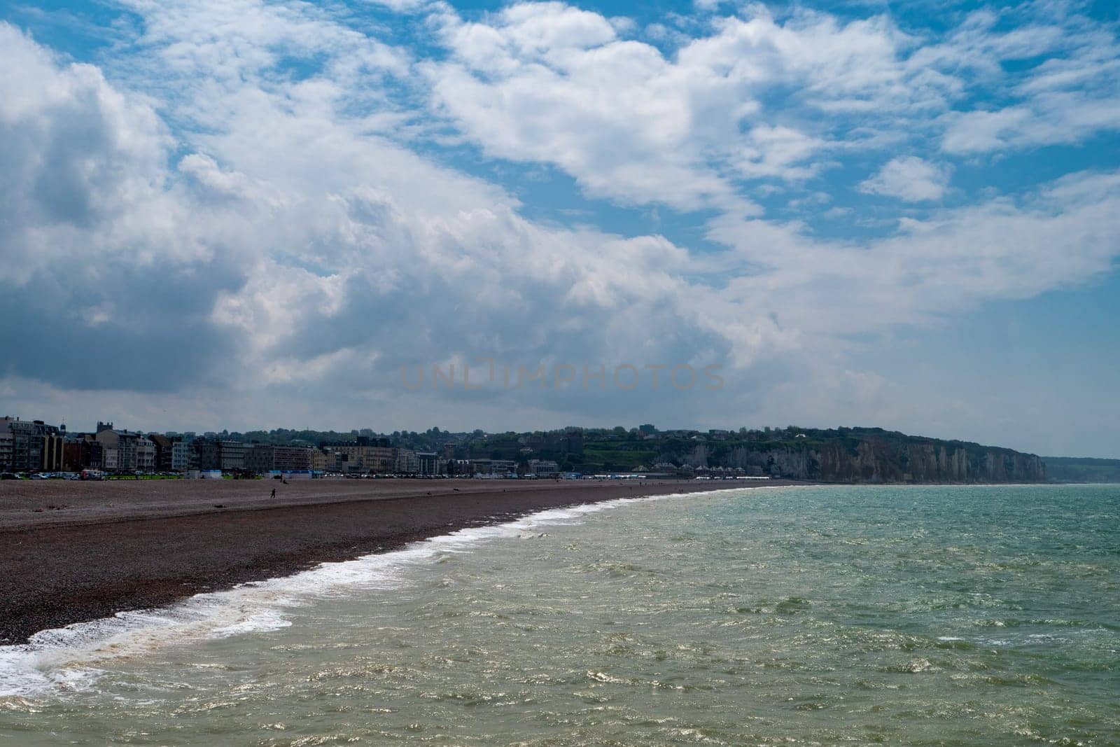 A beach with a cloudy sky in the background. The beach is empty and the water is calm, Dieppe, France