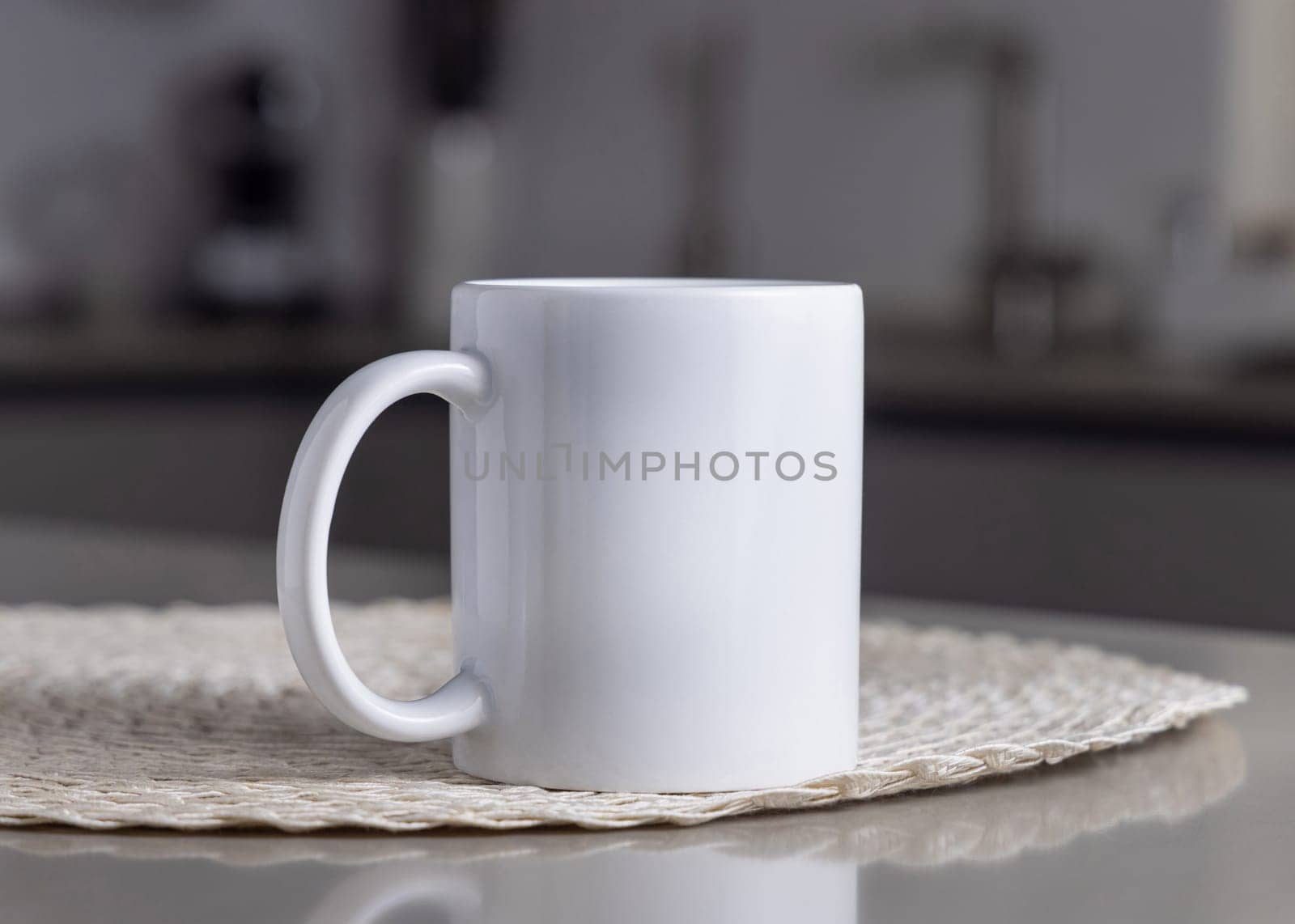 Closeup of 11 oz white blank coffee mug on grey kitchen table over blured modern kitchen grey interior, mockup. Template for your design or advertising with copy space