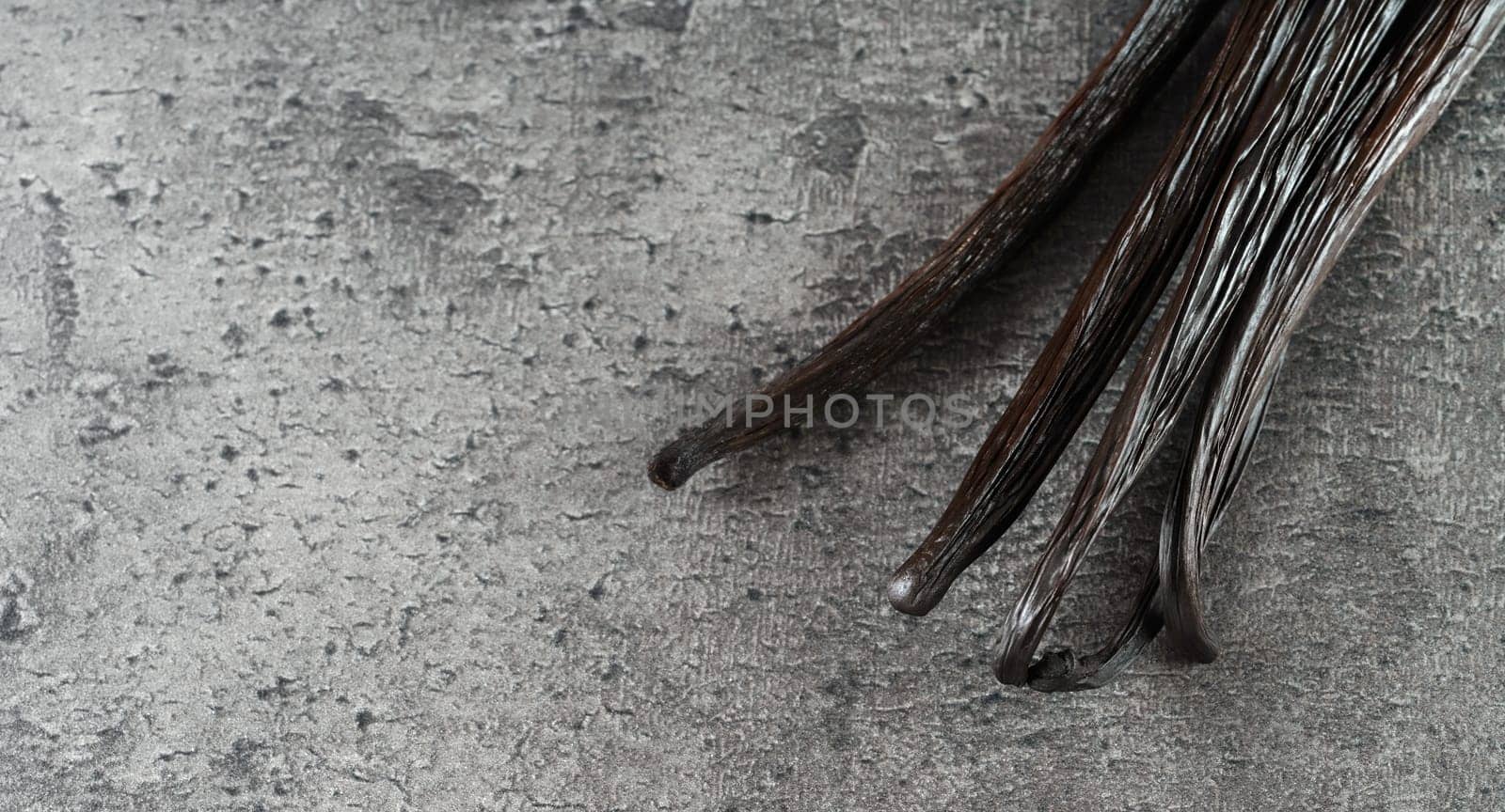 Four dark brown bourbon vanilla sticks on gray stone like board, empty space for text left side