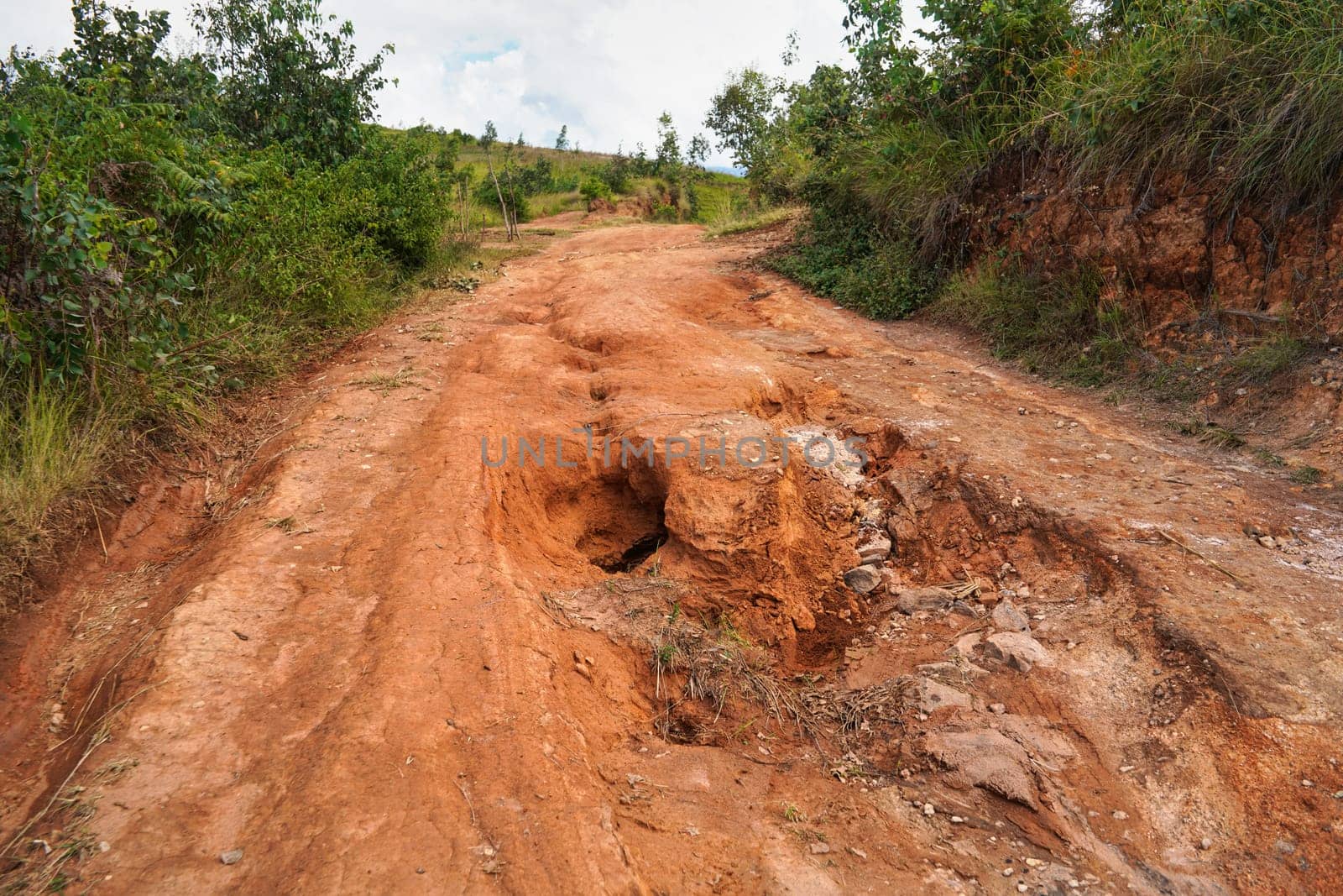 Red dust and mud road in poor condition with large holes and bumps formed after rain. Routes to Andringitra national park are extremely bad during wet season in region near Sendrisoa, Madagascar