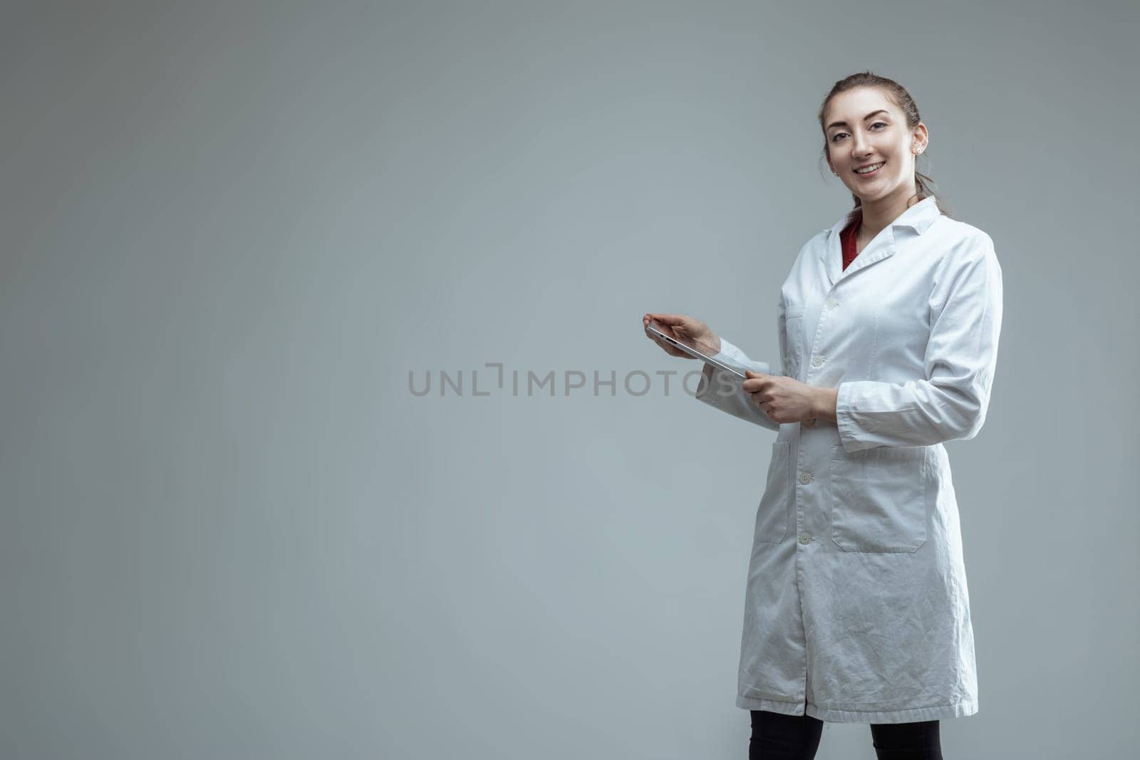 Young female scientist wearing a lab coat is holding a digital tablet, smiling at the camera, suggesting expertise in science, research, and engineering