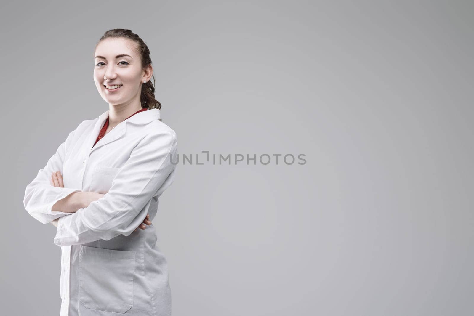 Portrait of a confident young female scientist smiling with crossed arms in a studio setting against a gray background, embodying professionalism and expertise in research