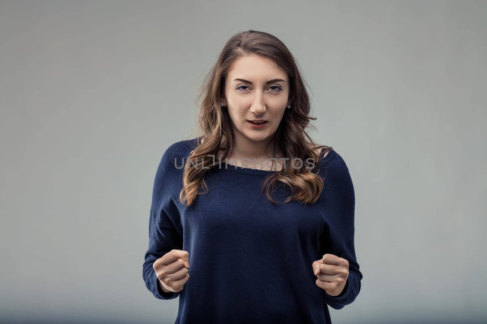 Portrait of a determined young woman clenching her fists, conveying strength, willpower, and a readiness to overcome challenges with a serious facial expression